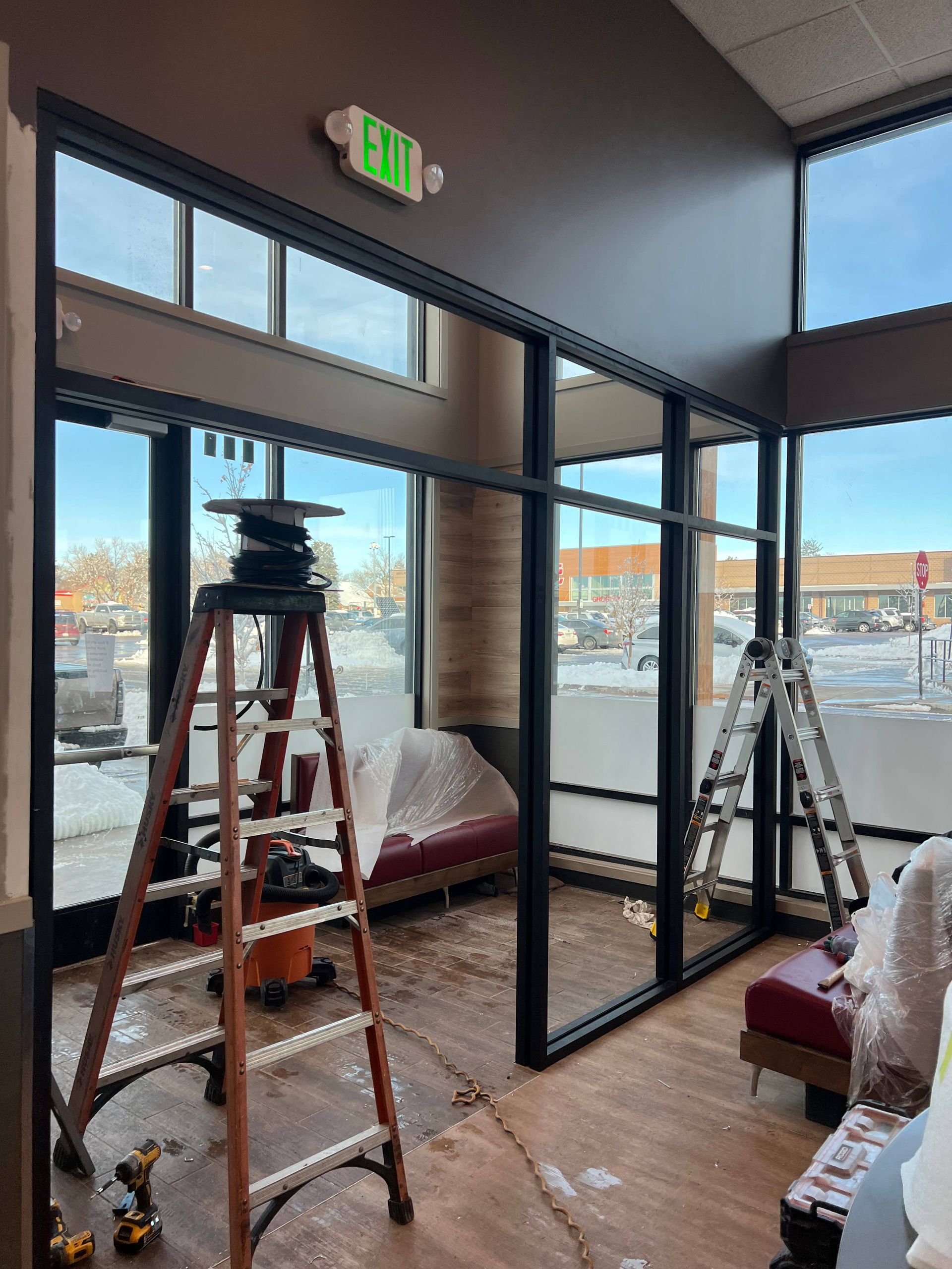Interior construction: Black framed glass wall, ladders, tools, brown and tan walls, snow outside windows.