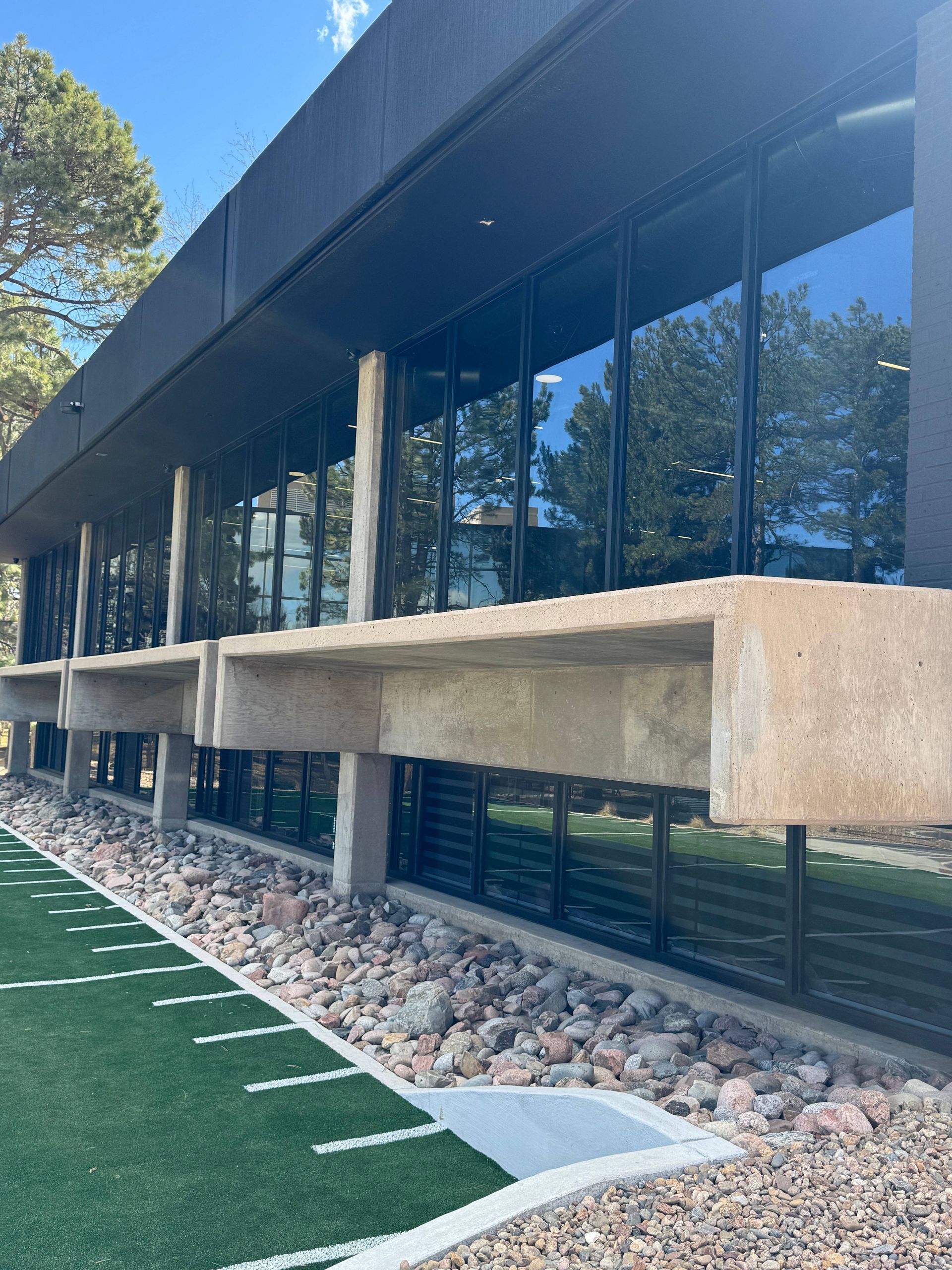 Modern building with large windows, concrete overhangs, set in a rocky area with artificial turf.