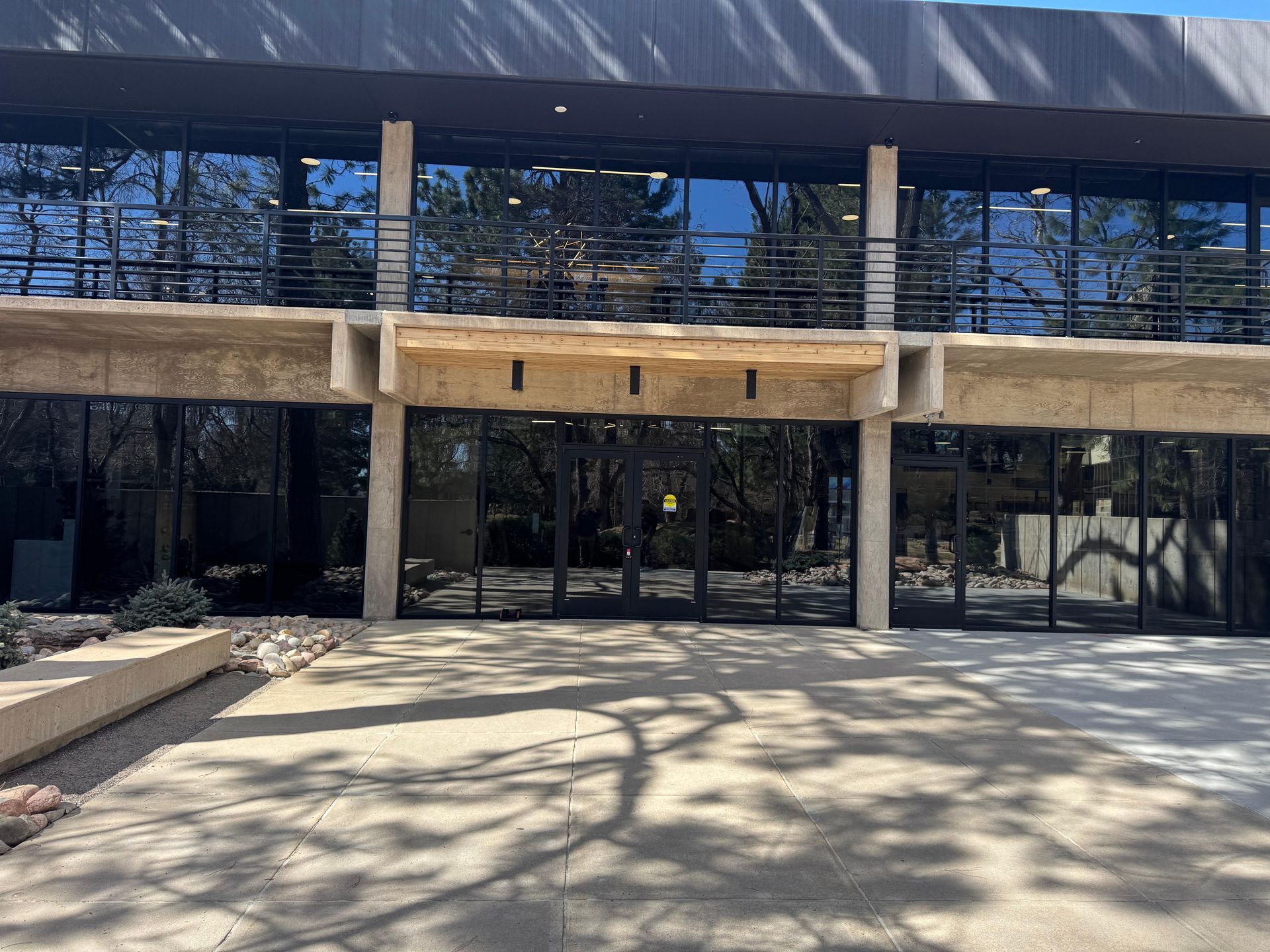 Building entrance with glass doors and reflective windows. Concrete overhang. Outdoors in sunlight.