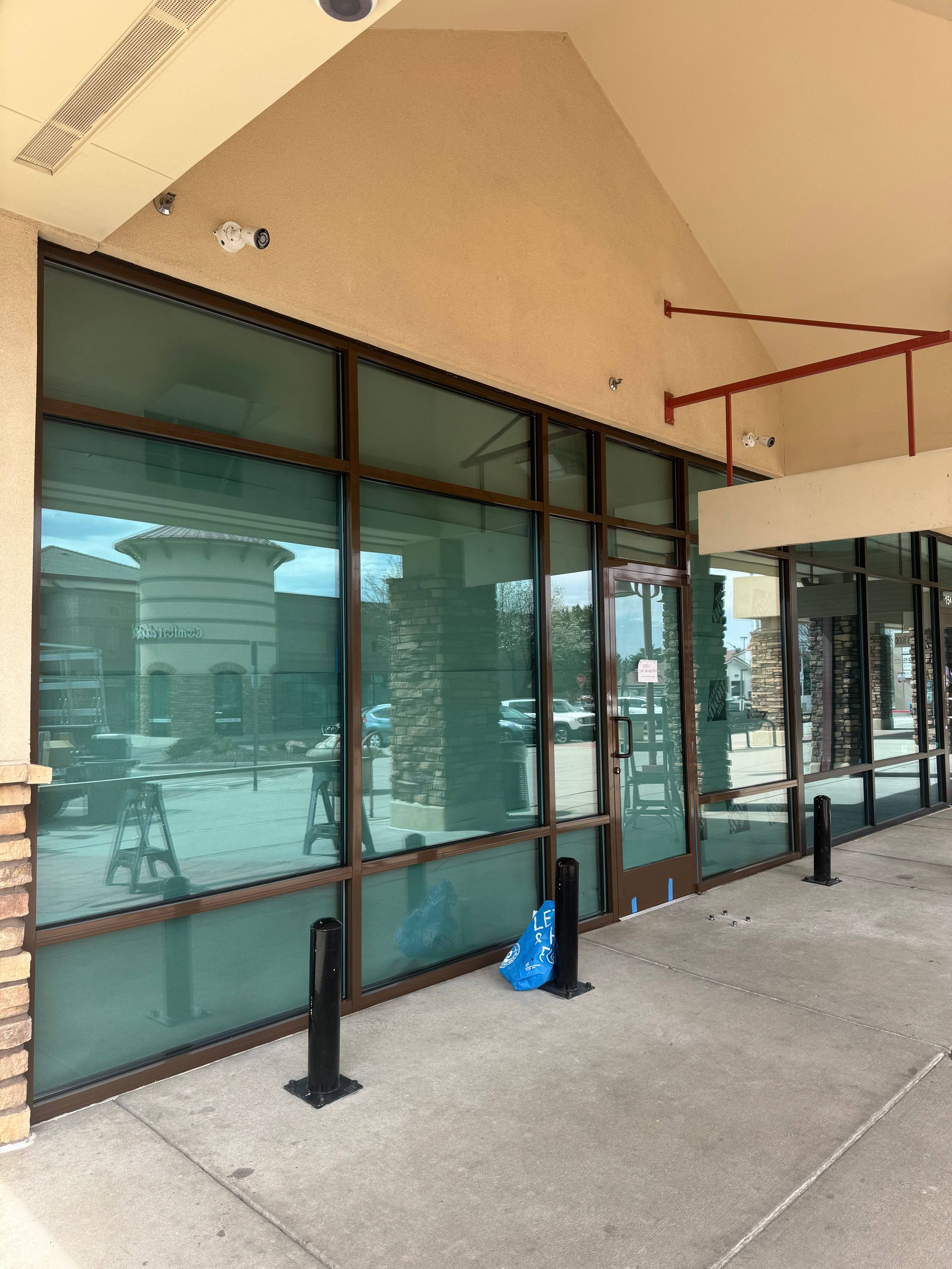 Storefront with large glass windows, brown frames, and a covered walkway.