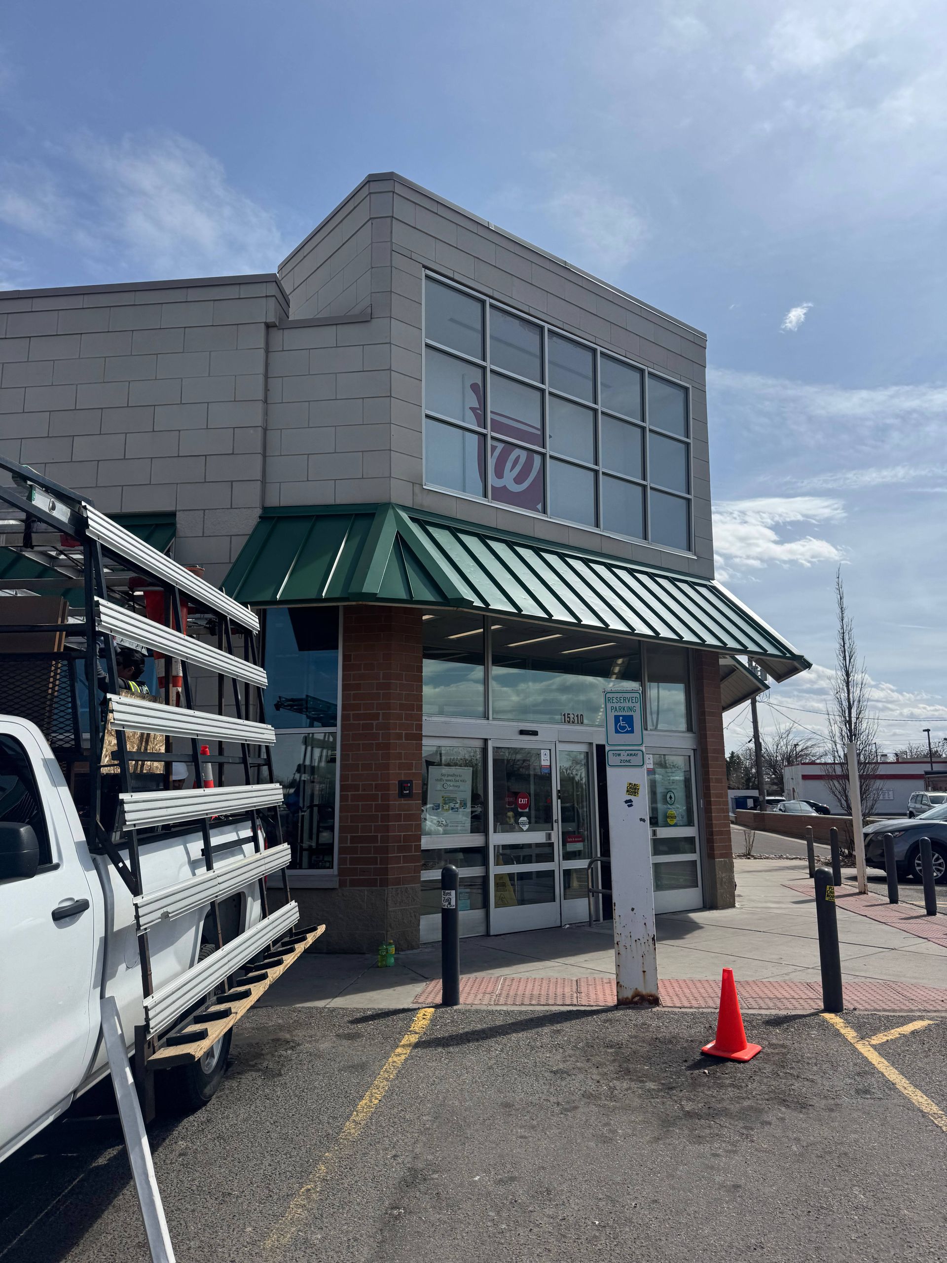Walgreens exterior with accessible entrance, handicap sign. Green roof, brick columns, gray building, sunny day.