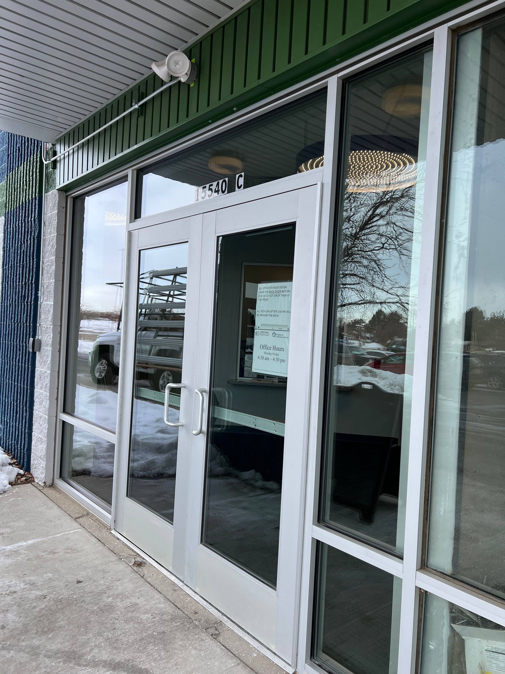 Glass front doors with white frames, on a building with a green awning. Snowy ground.