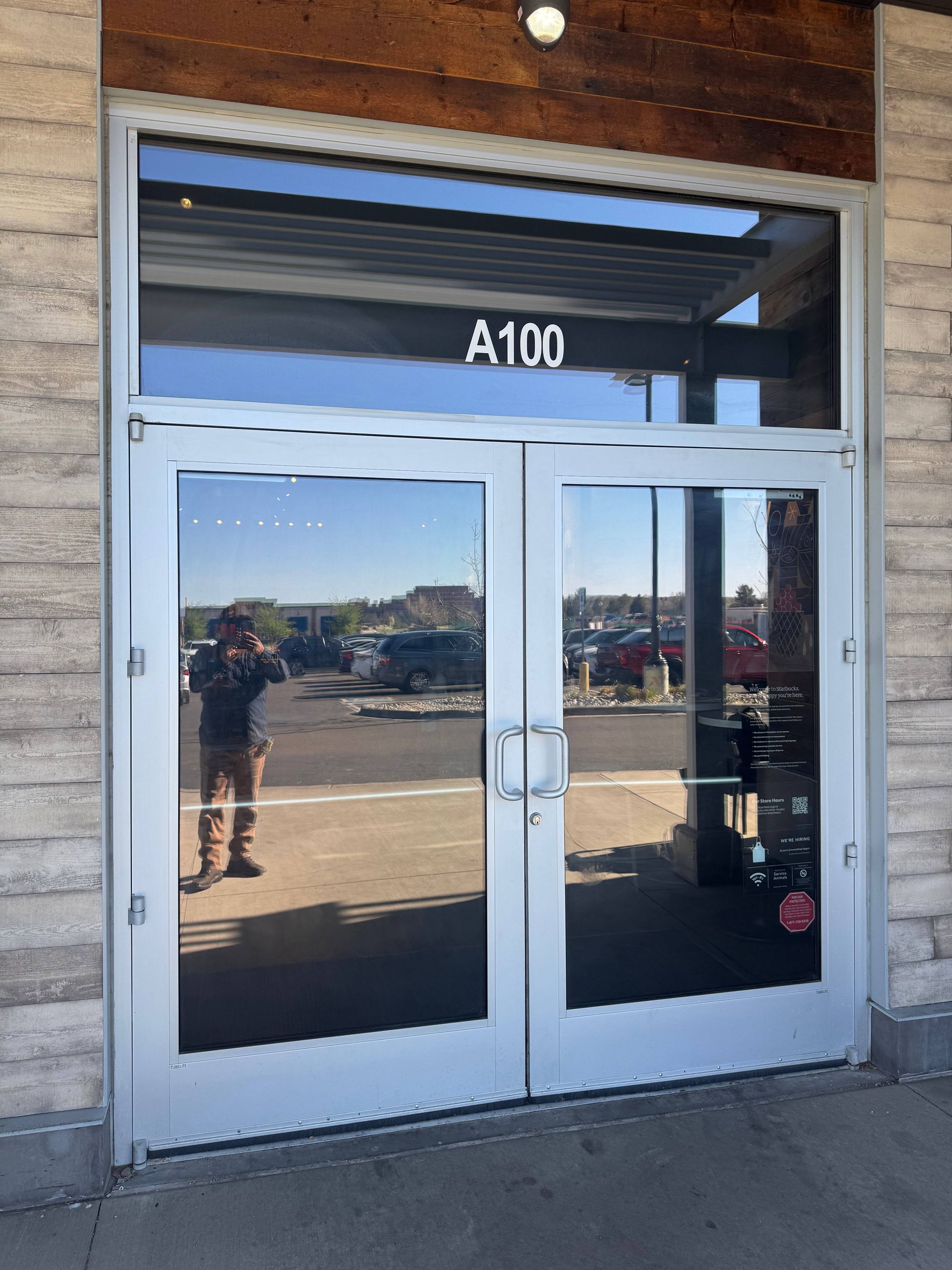 Double glass doors with the number A100 above, reflecting a person taking a photo outside a building.