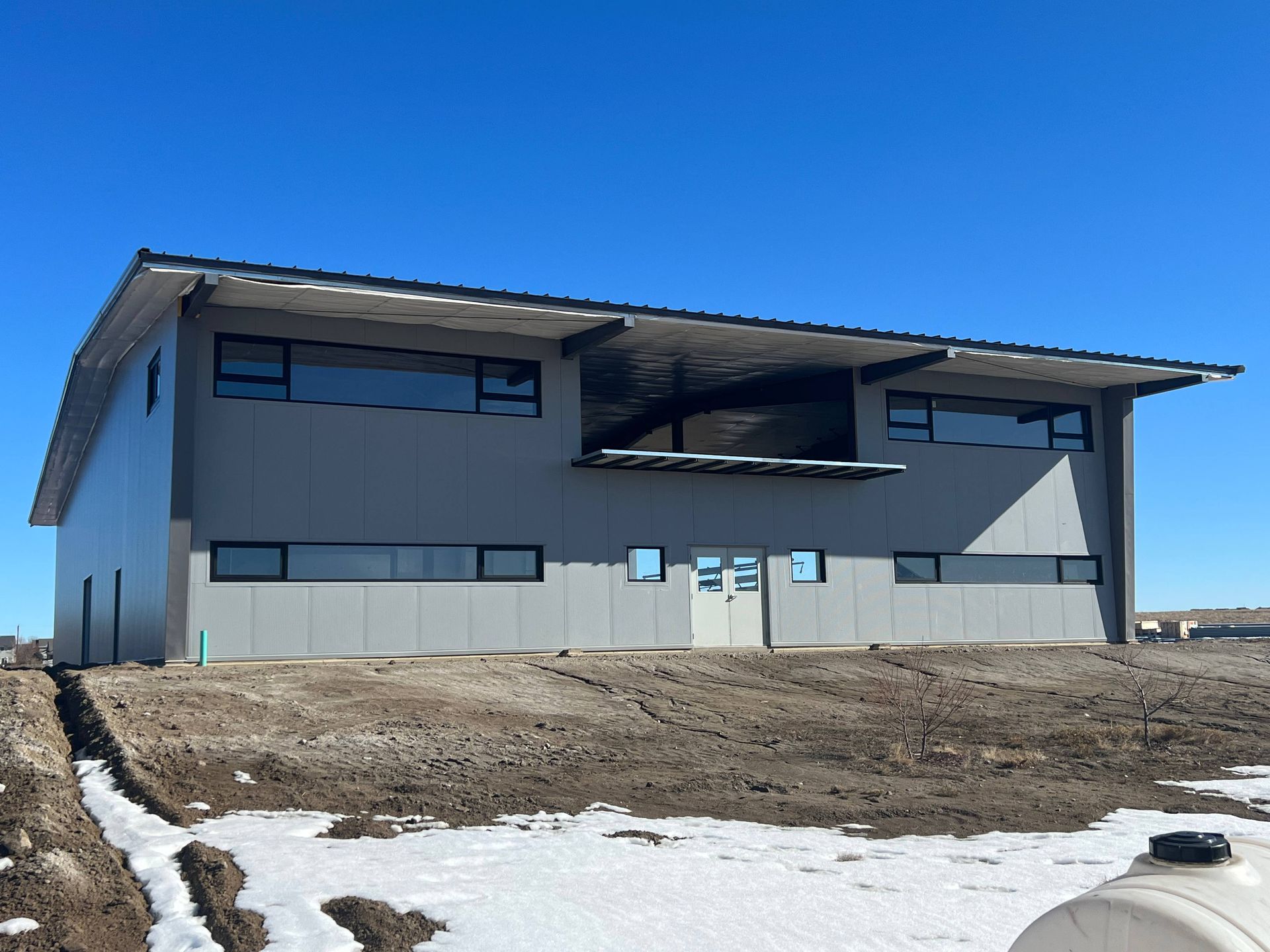 Two-story modern gray building with large windows and a dark roof, set against a clear blue sky.