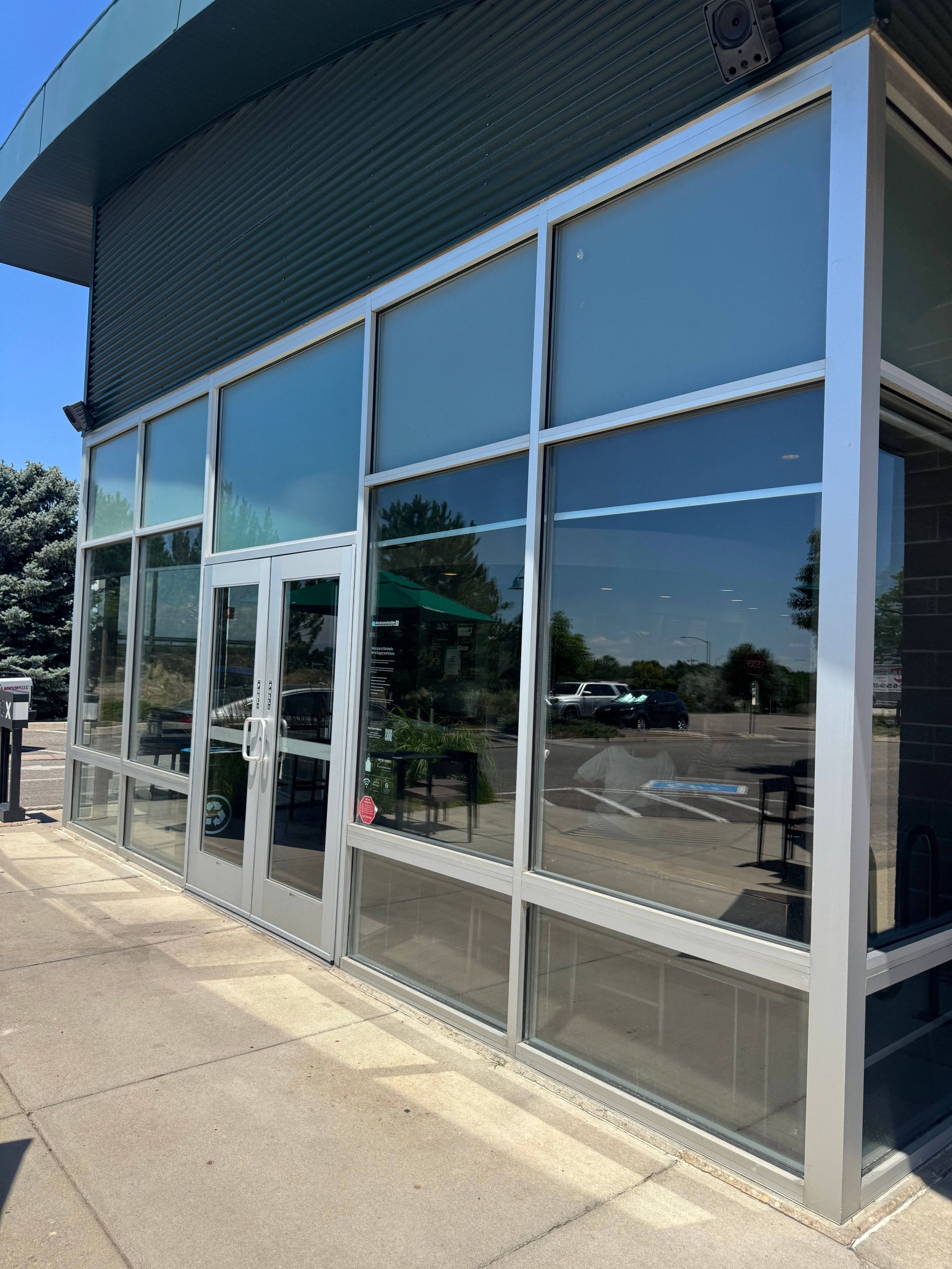 Exterior of a building with large glass windows and door, silver frames, and a sidewalk.