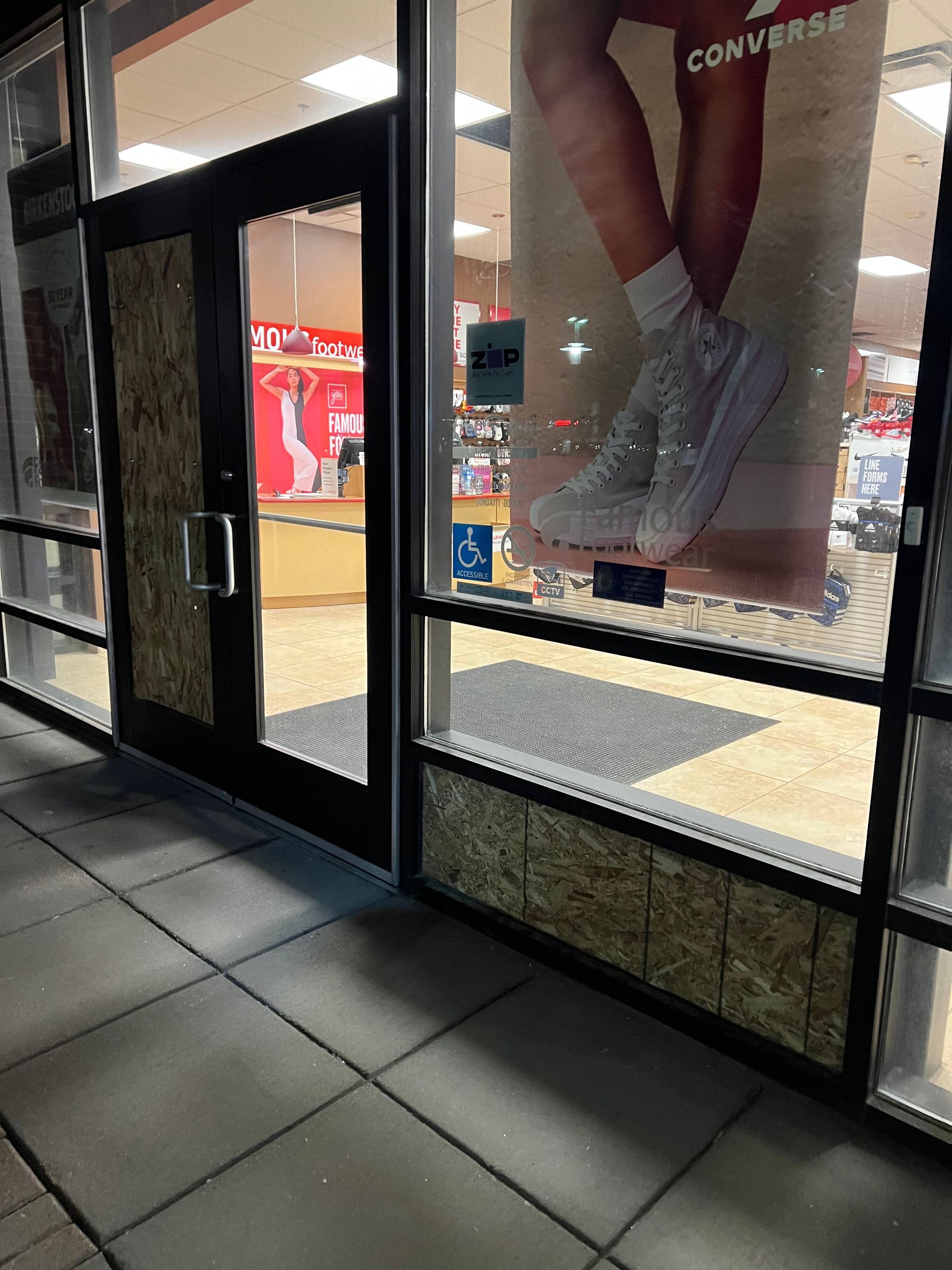 Storefront with boarded-up windows and door. A Converse shoe ad is visible. Sidewalk in front.