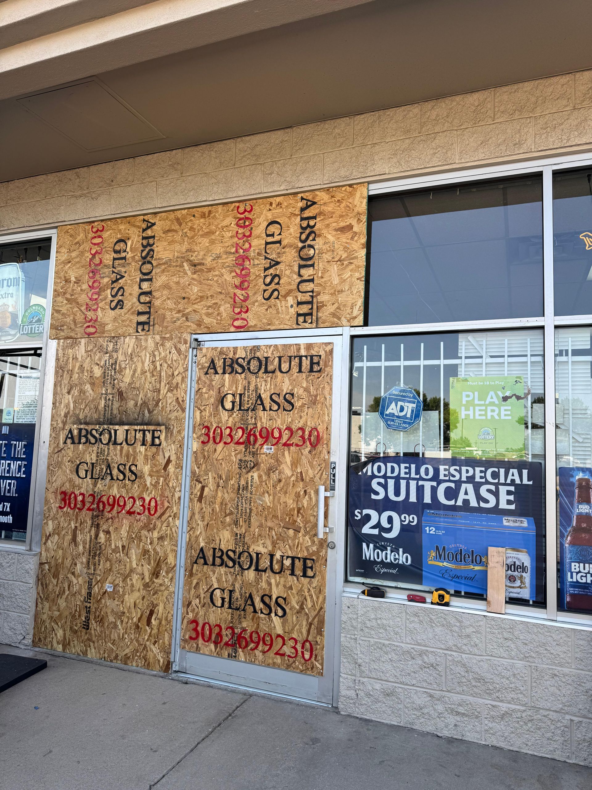 Building exterior with plywood covering a door and window, business named Absolute Glass.