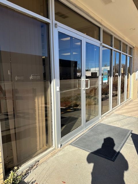 Glass entrance doors with silver frames; a grey mat sits outside.