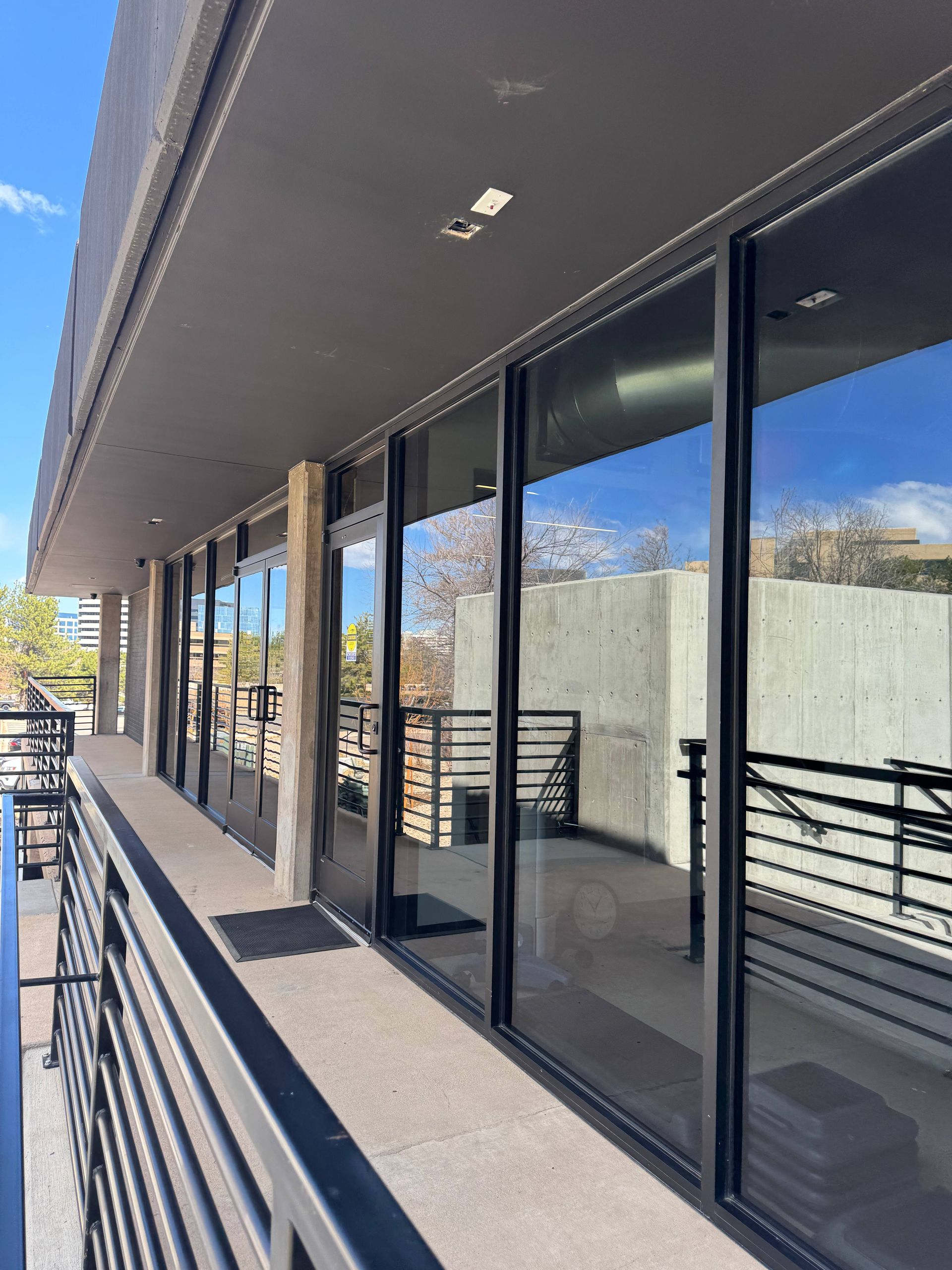 Exterior view of a building with large glass windows reflecting the sky and a balcony with black railings.
