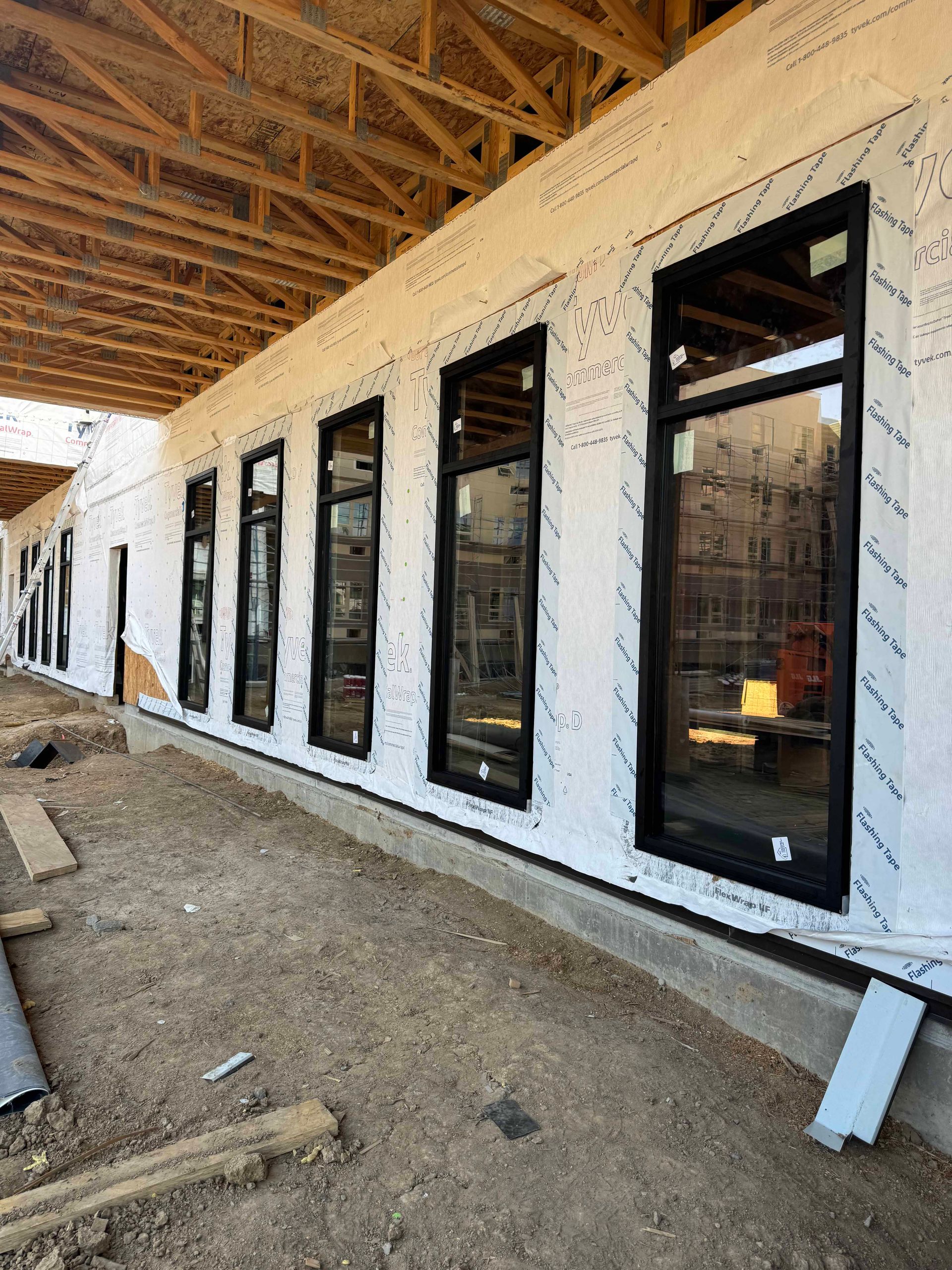 Construction site: exterior wall with black-framed windows, covered in white sheeting, wood beams overhead.