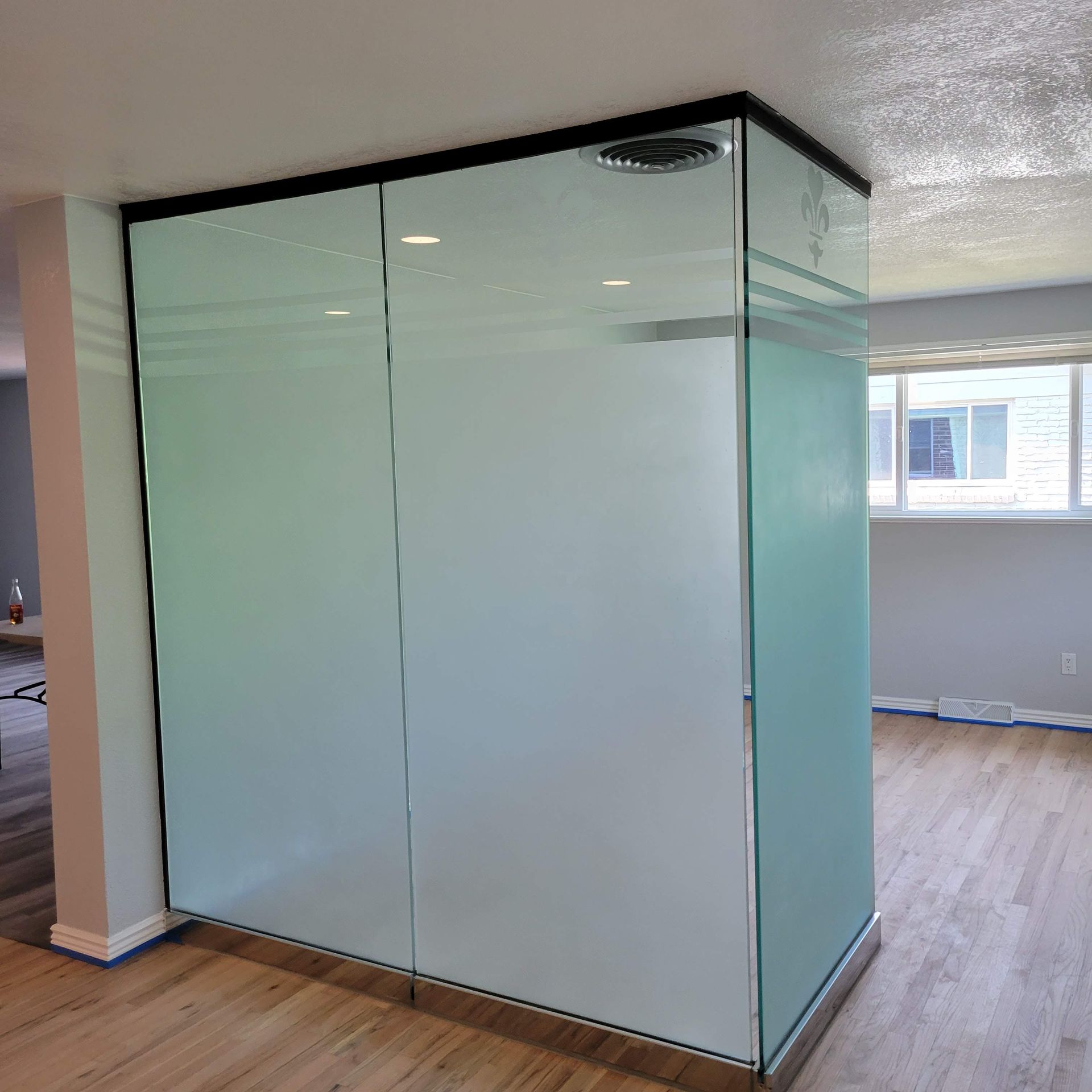 Frosted glass shower enclosure with black trim, in a room with wooden floors and a window.