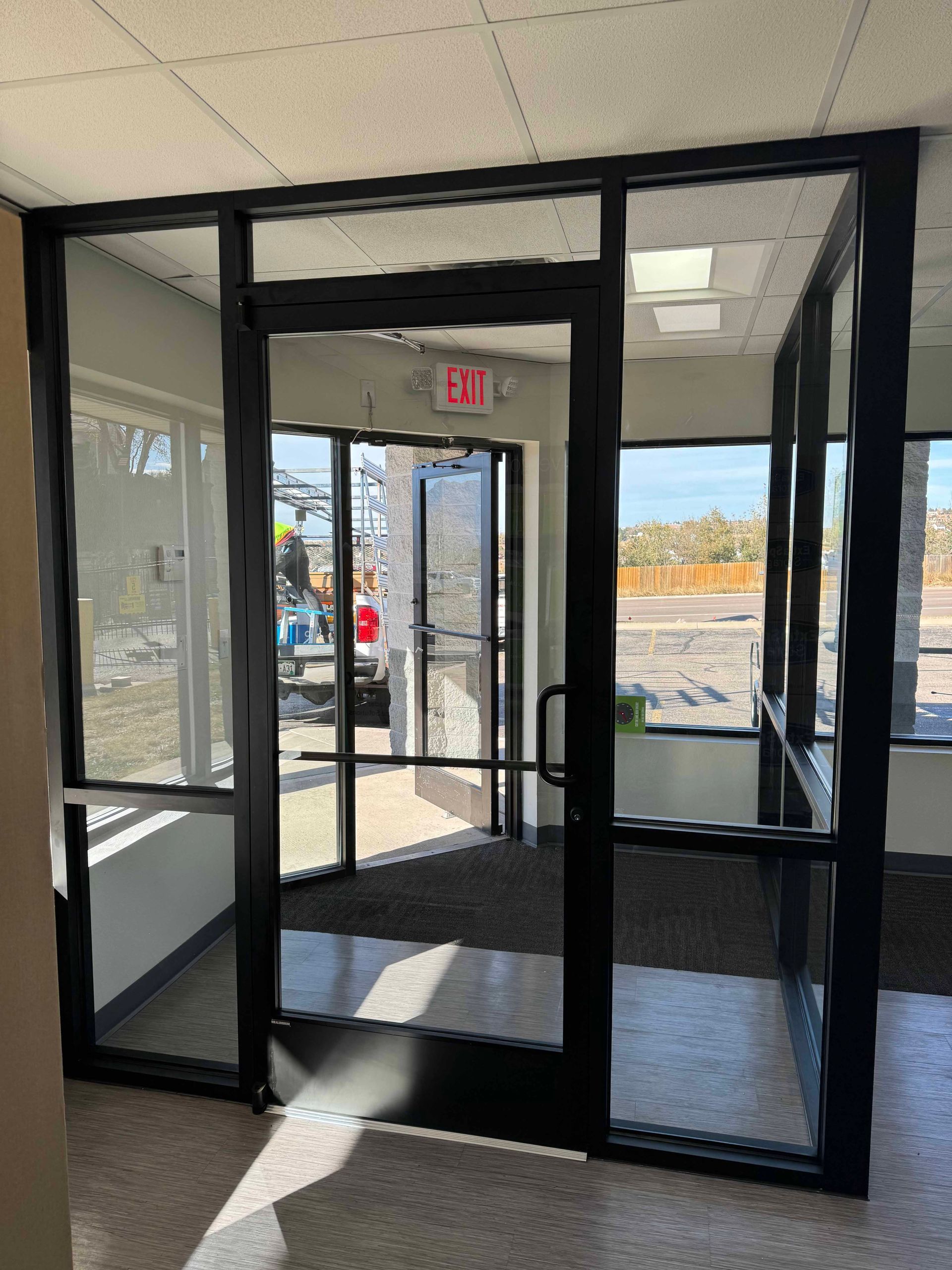 Black framed glass doors and sidelights leading to an outdoor area; exit sign visible.