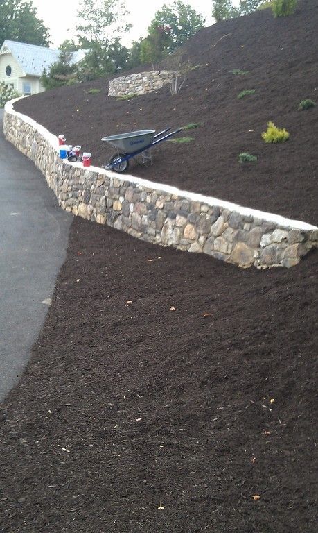 Stone retaining wall on a hillside with wheelbarrow and fresh mulch.