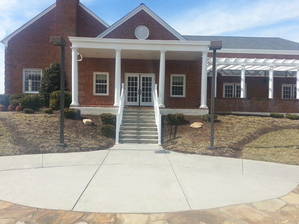 Brick building with white pillars, steps to double doors, and a pergola on the right.