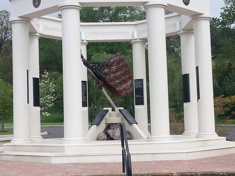 War memorial with American flag, white pillars, black plaques, and stone base.