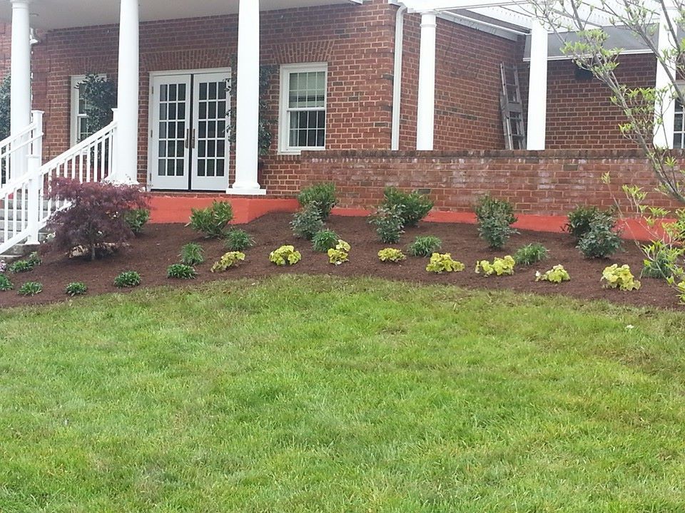 House with brick facade, white columns, and newly planted garden bed with mulch and shrubs.