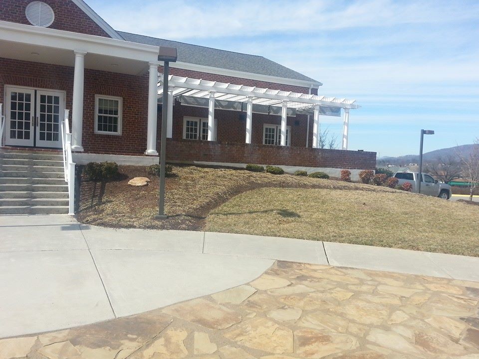 Brick building with white columns, pergola, and steps. Lawn and sidewalk in the foreground; blue sky.