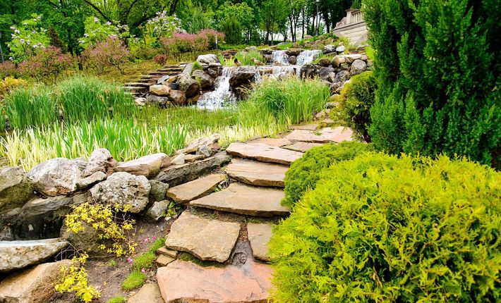 A stone path in a garden with a waterfall in the background.