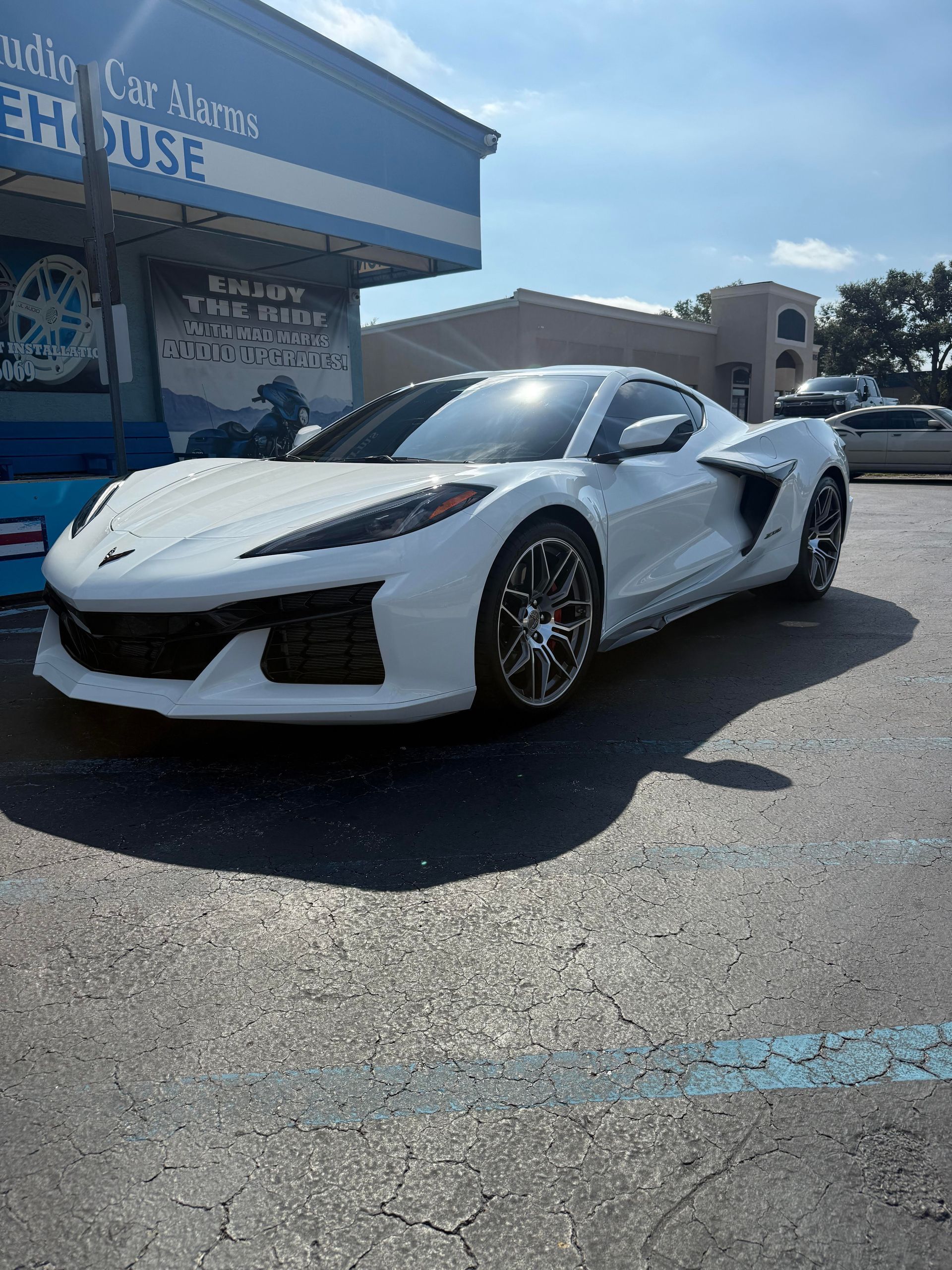 White sports car parked in front of a blue building with car service signage on a sunny day.