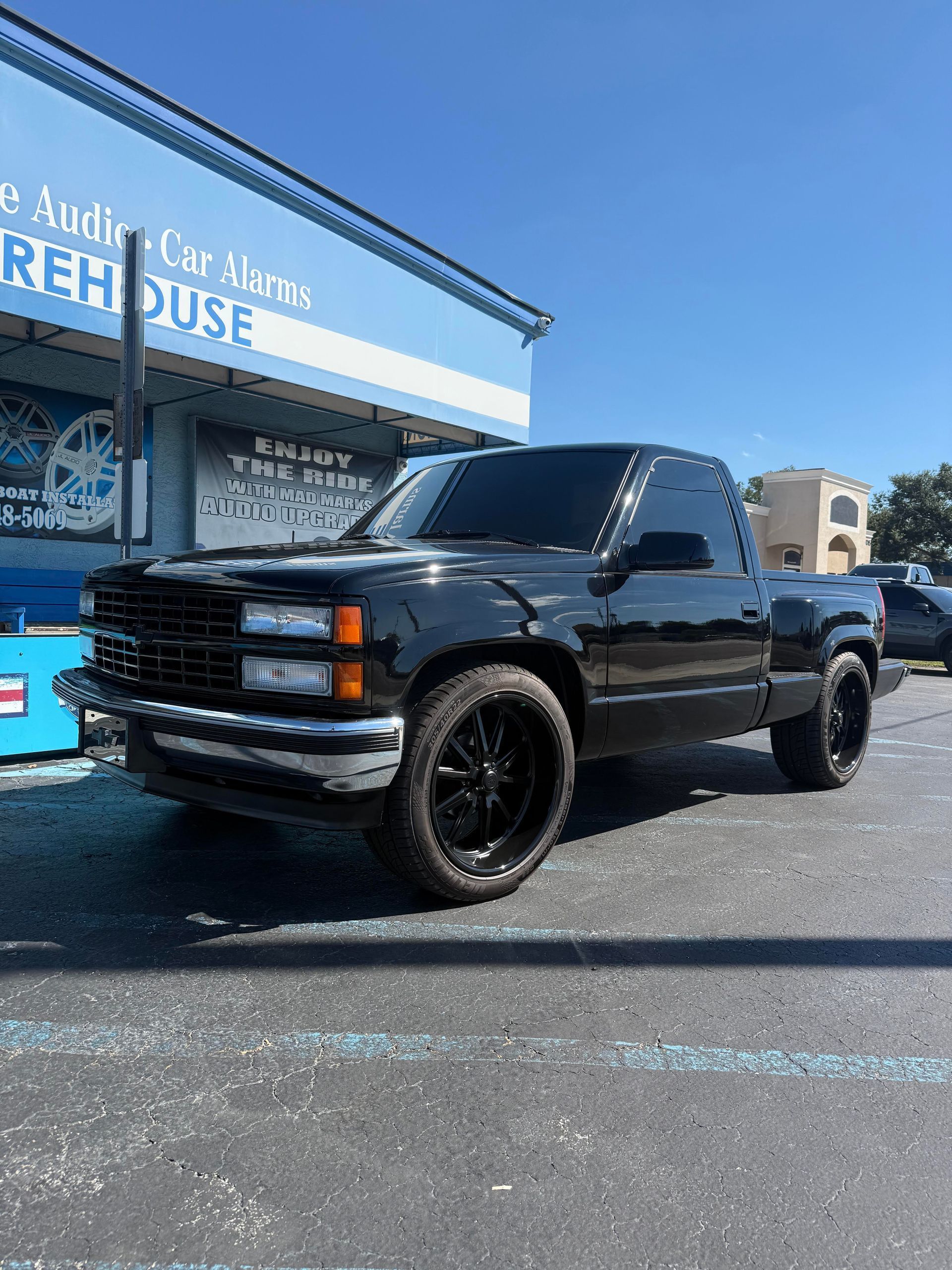 Black Chevrolet pickup truck with black rims parked outside a store with a blue awning.