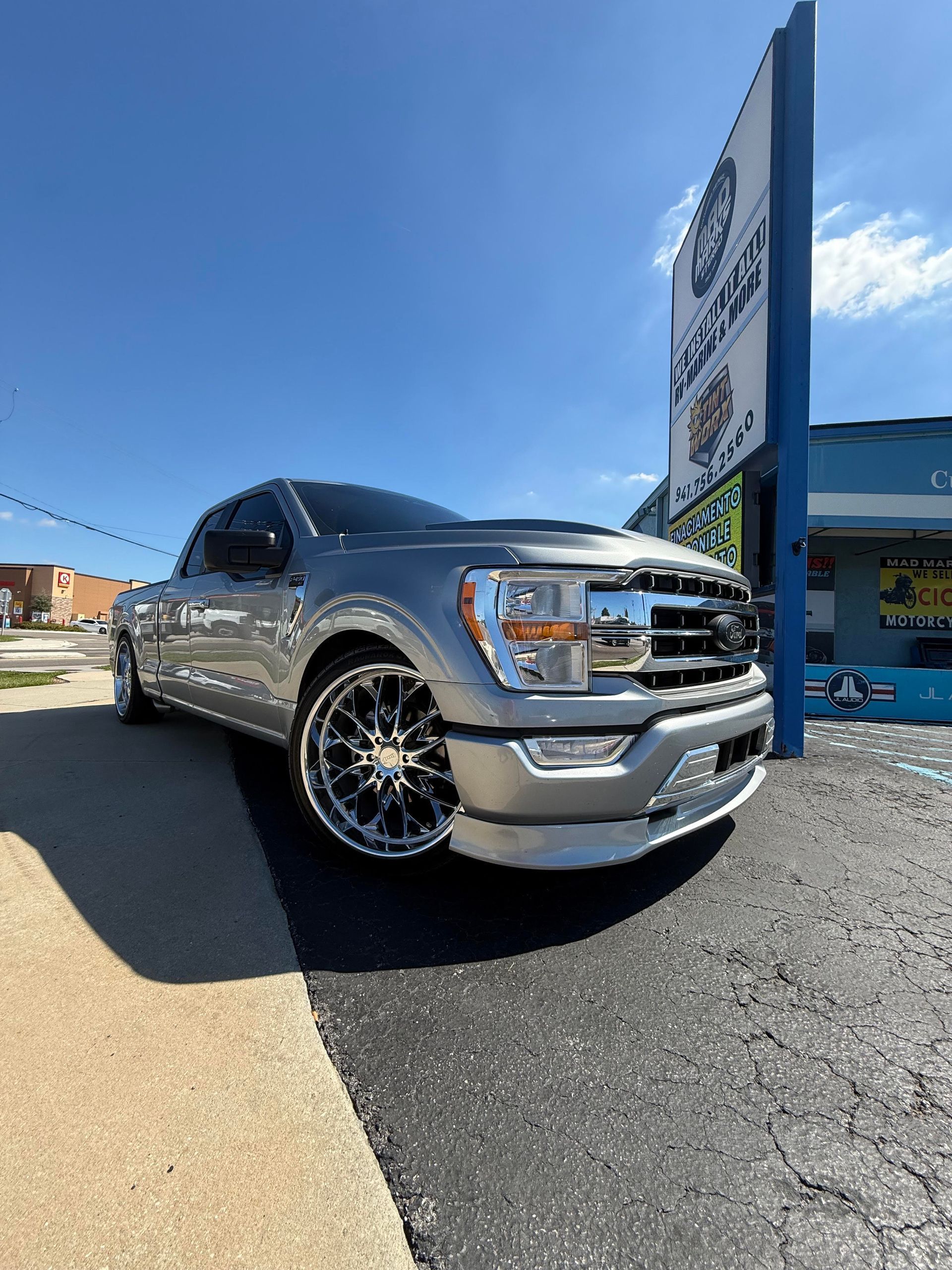 Silver Ford pickup truck parked in front of a blue building with a sign on a sunny day.