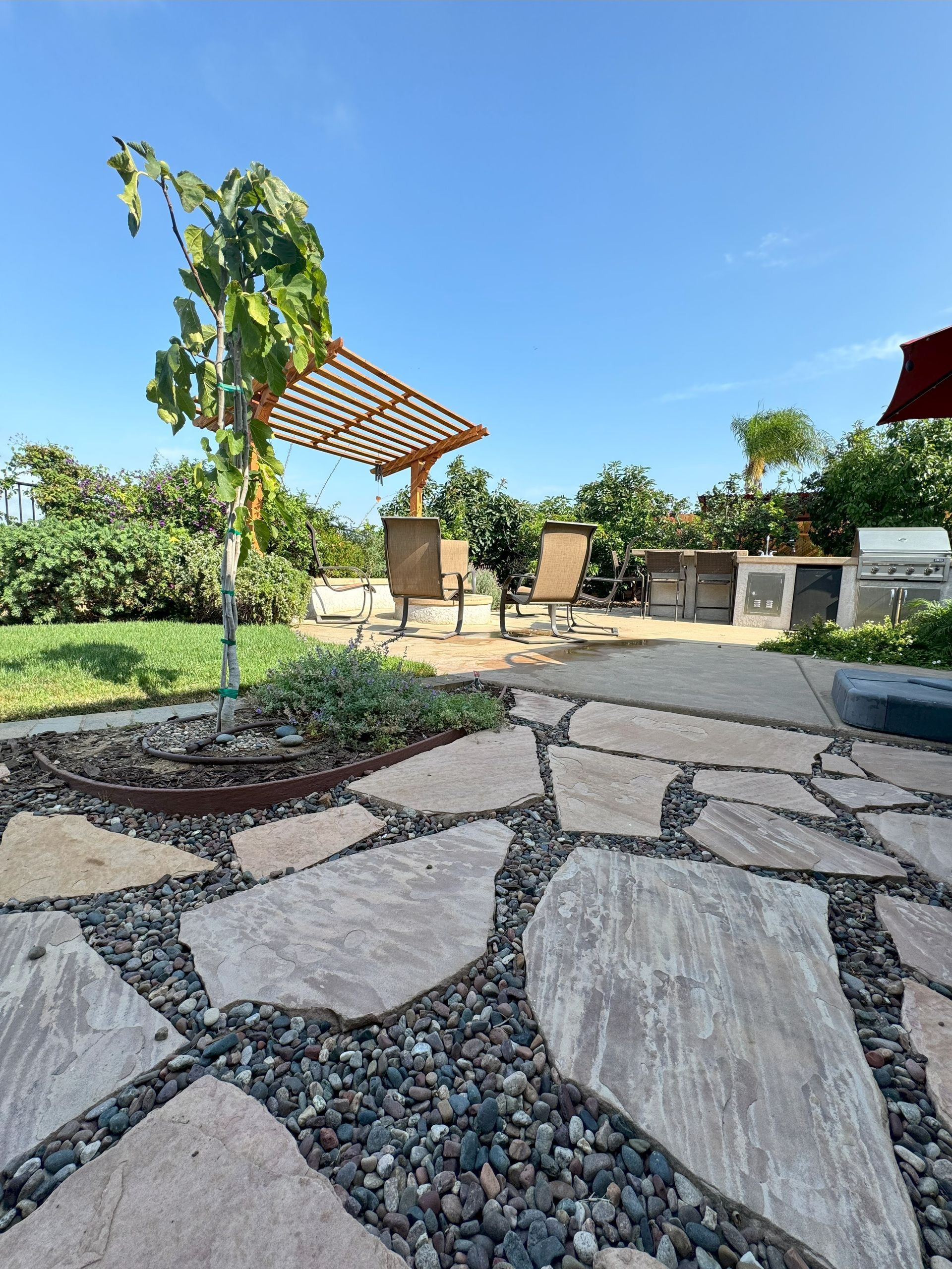 A stone patio with a pergola and chairs in the background