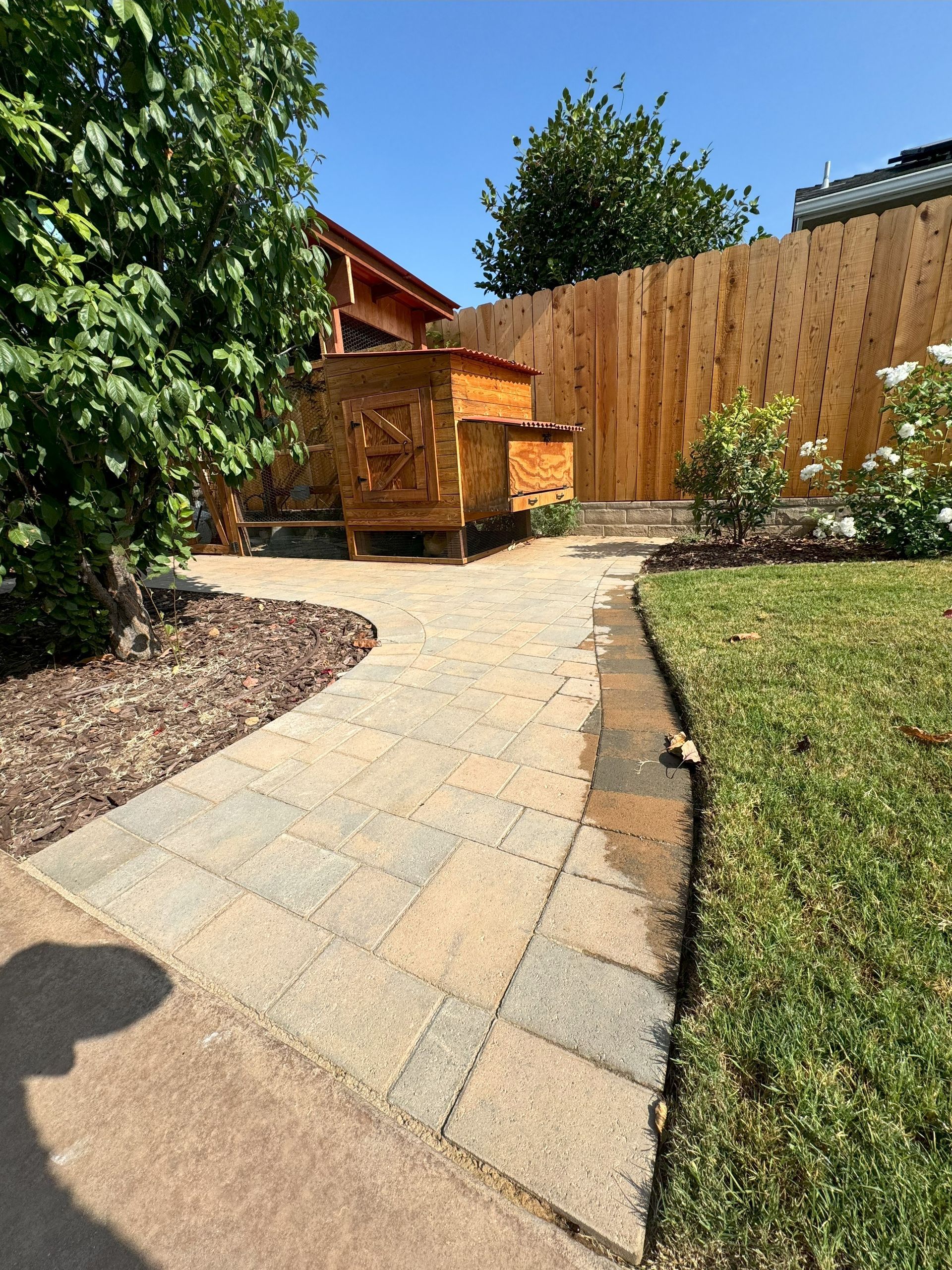 A brick walkway leads to a wooden fence in a backyard