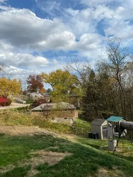 Overlooking a yard and neighborhood on a partly cloudy autumn day. Trees show red, yellow, and green leaves.