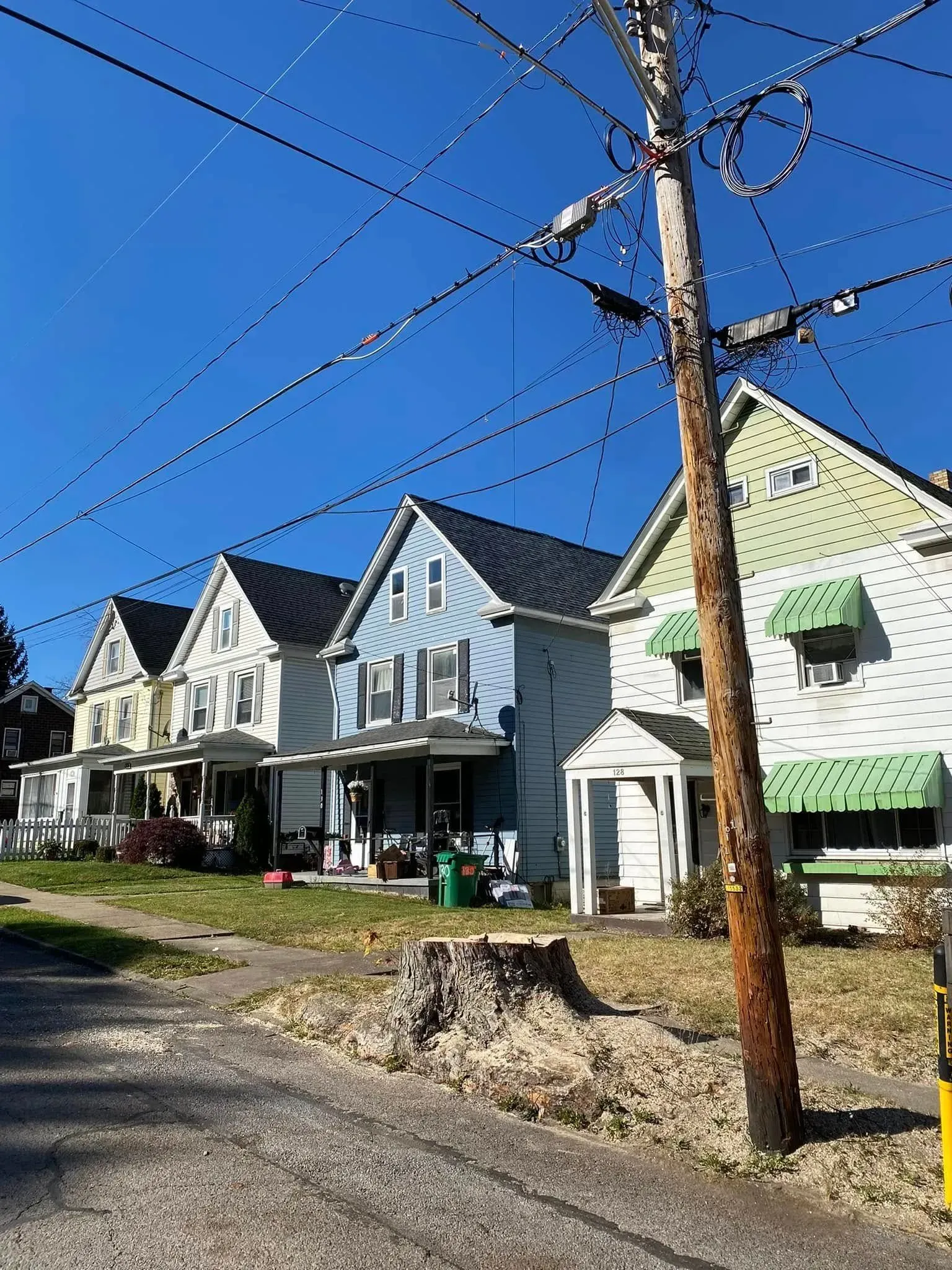 Row of colorful houses under a clear blue sky, with a utility pole in the foreground and tree stump.