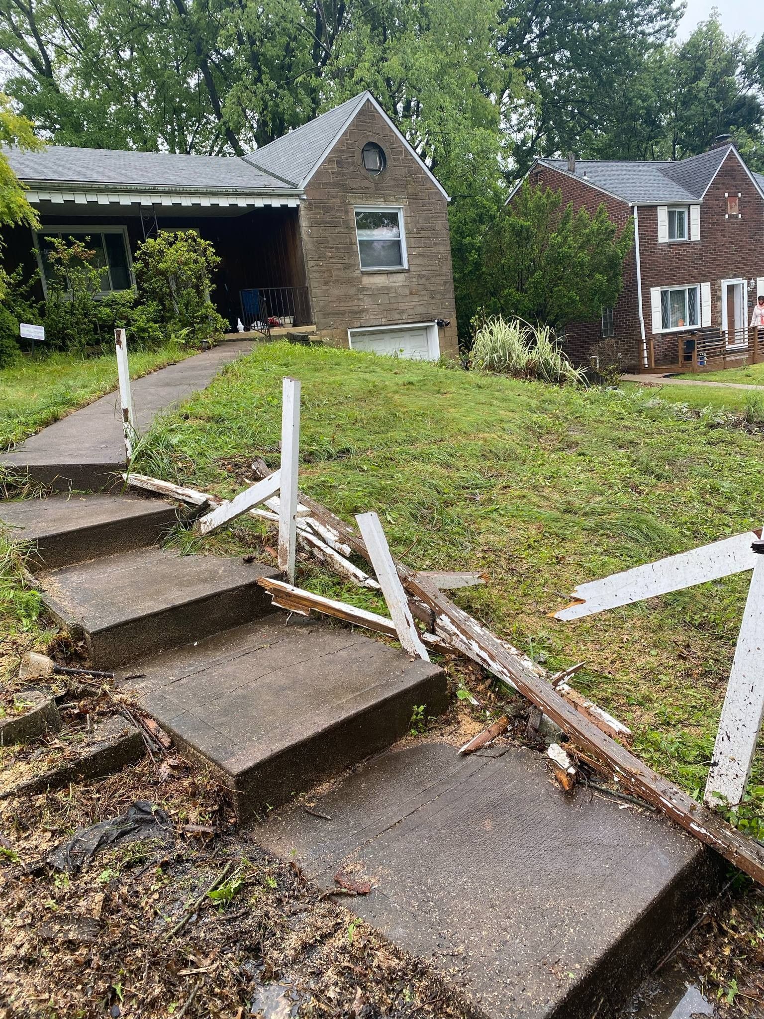 Steps leading up to a brick house with broken railing, overgrown lawn.