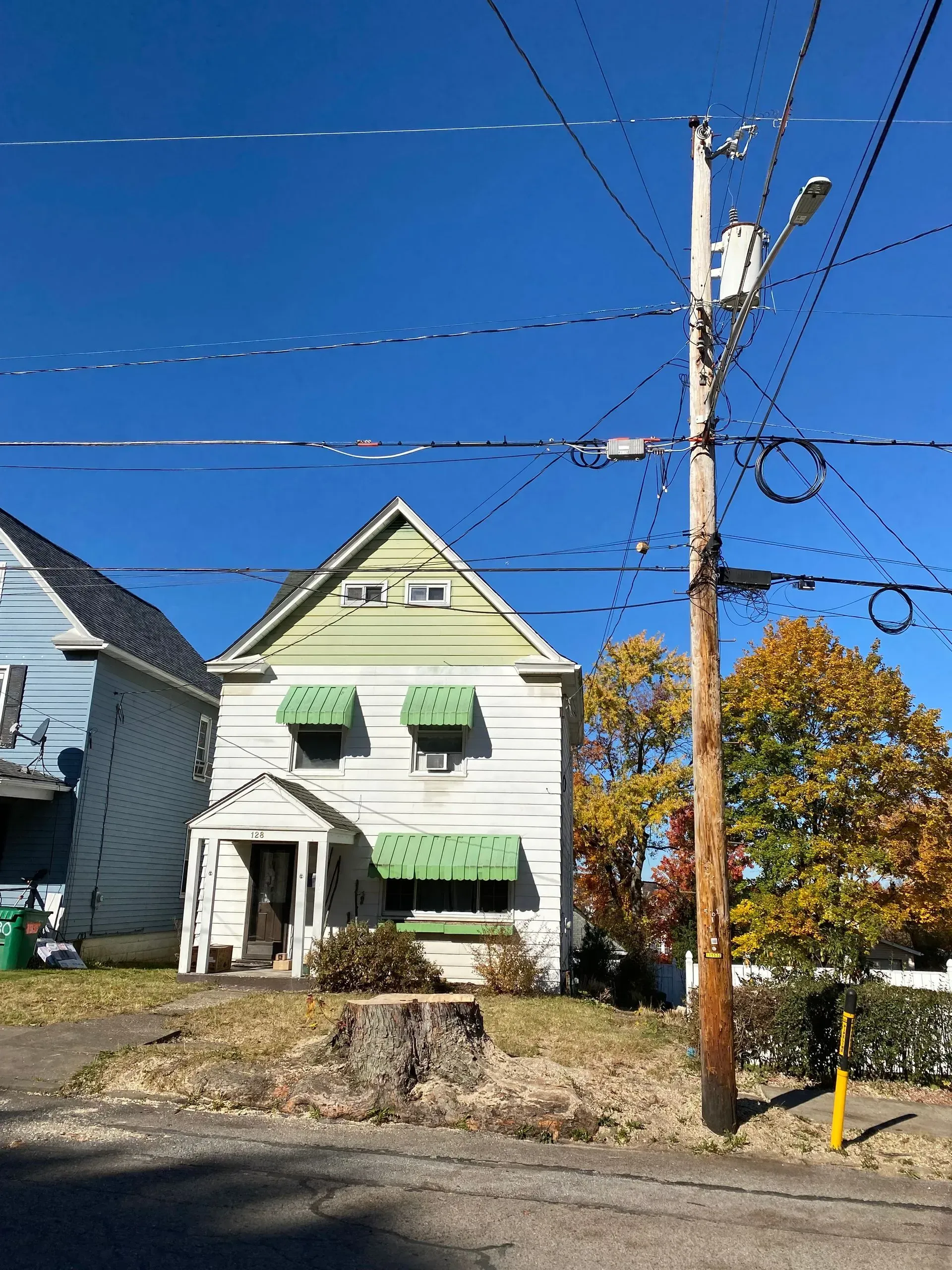 Two-story white house with green awnings, telephone pole on a sunny day.