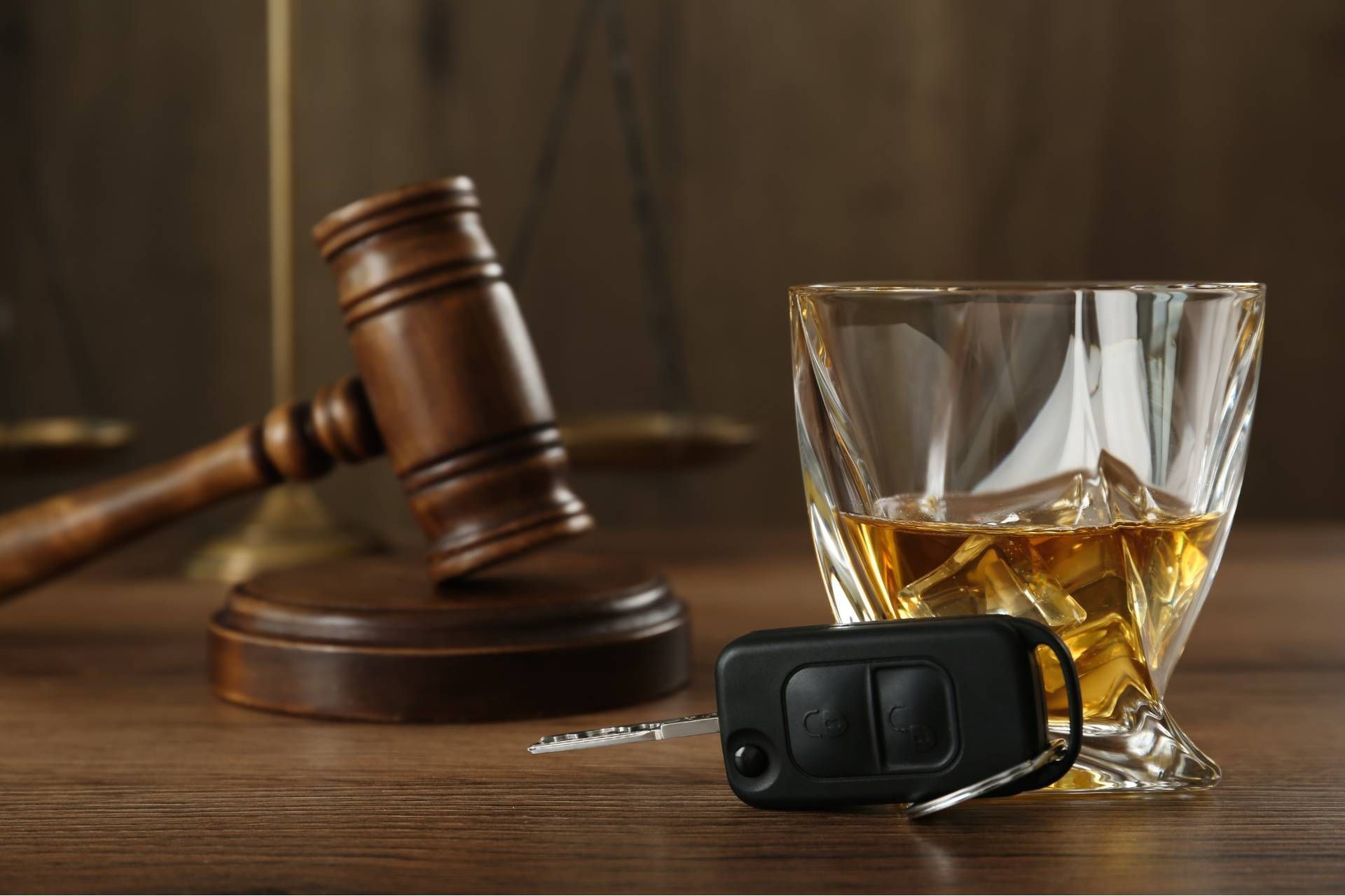 A glass of whiskey , a car key , and a judge 's gavel on a wooden table.