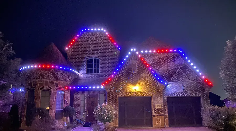 House at night outlined with red, white, and blue holiday lights around the roof and garage.