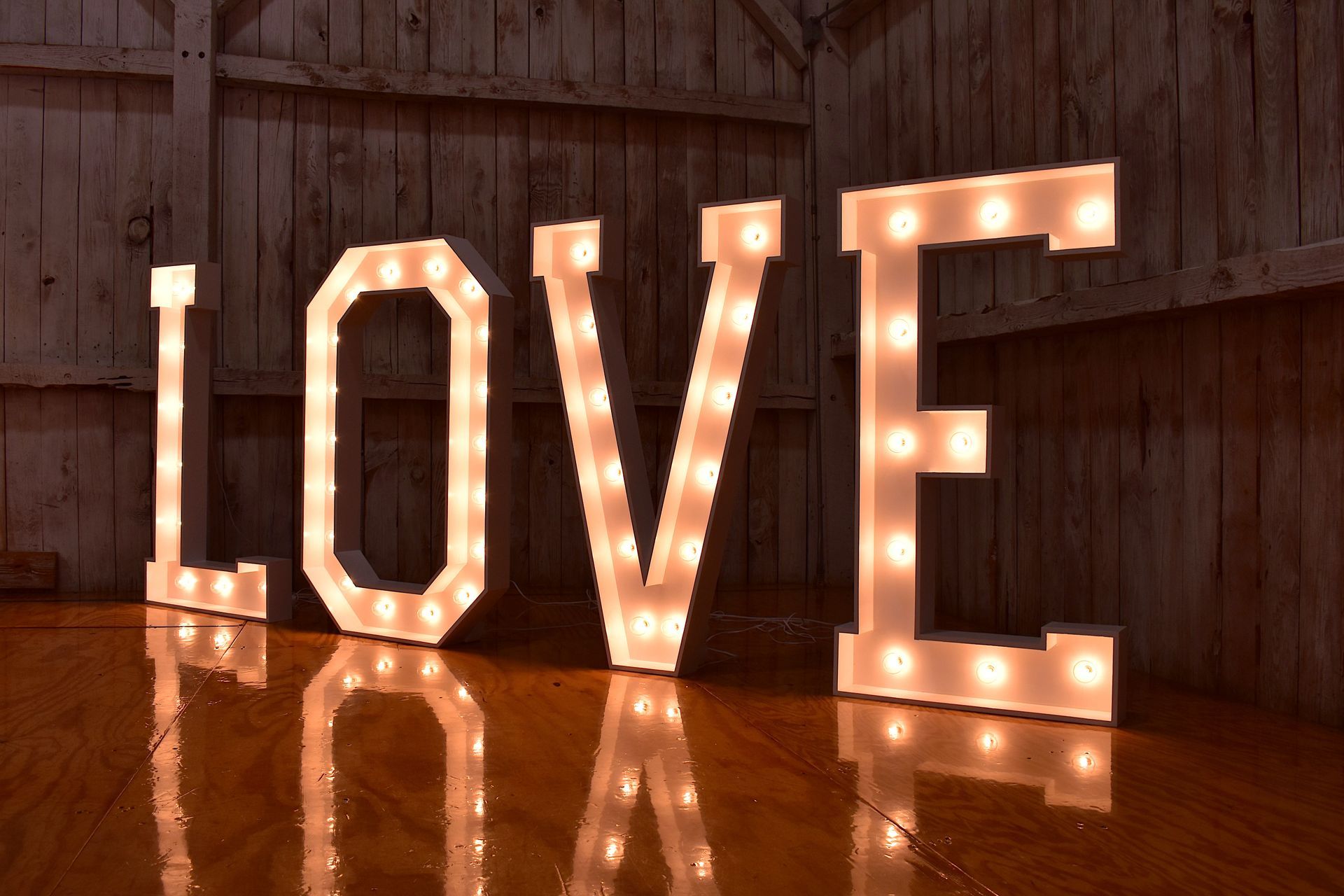 Marquee letters spelling LOVE glow warmly on a wooden floor, reflected in the polished surface.