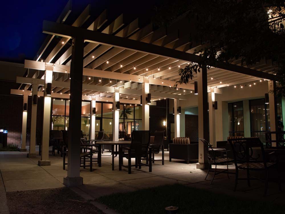 Outdoor patio dining area at night with warm lights, tables, chairs, and a wooden pergola.