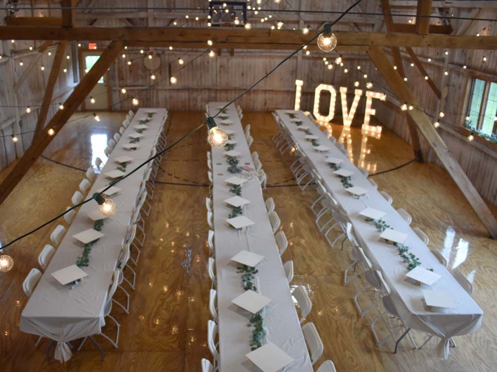 Rustic barn wedding reception with long tables, white chairs, and glowing LOVE sign