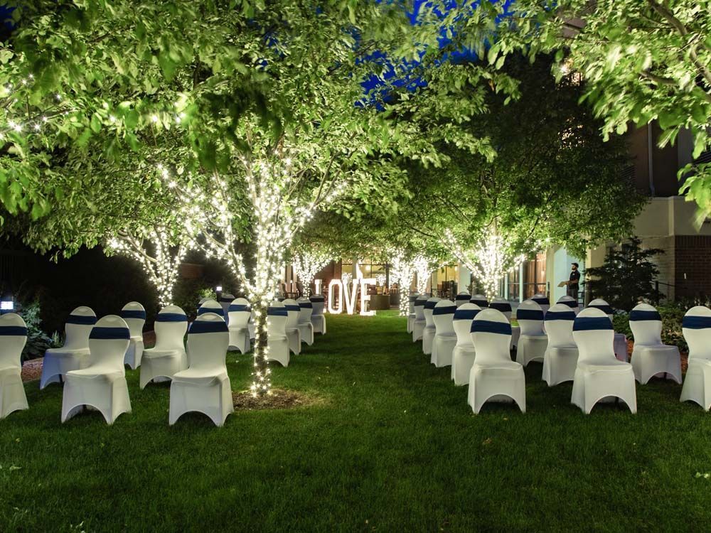 Outdoor wedding reception setup on a lawn with white chairs, trees lit by lights, and a glowing LOVE sign