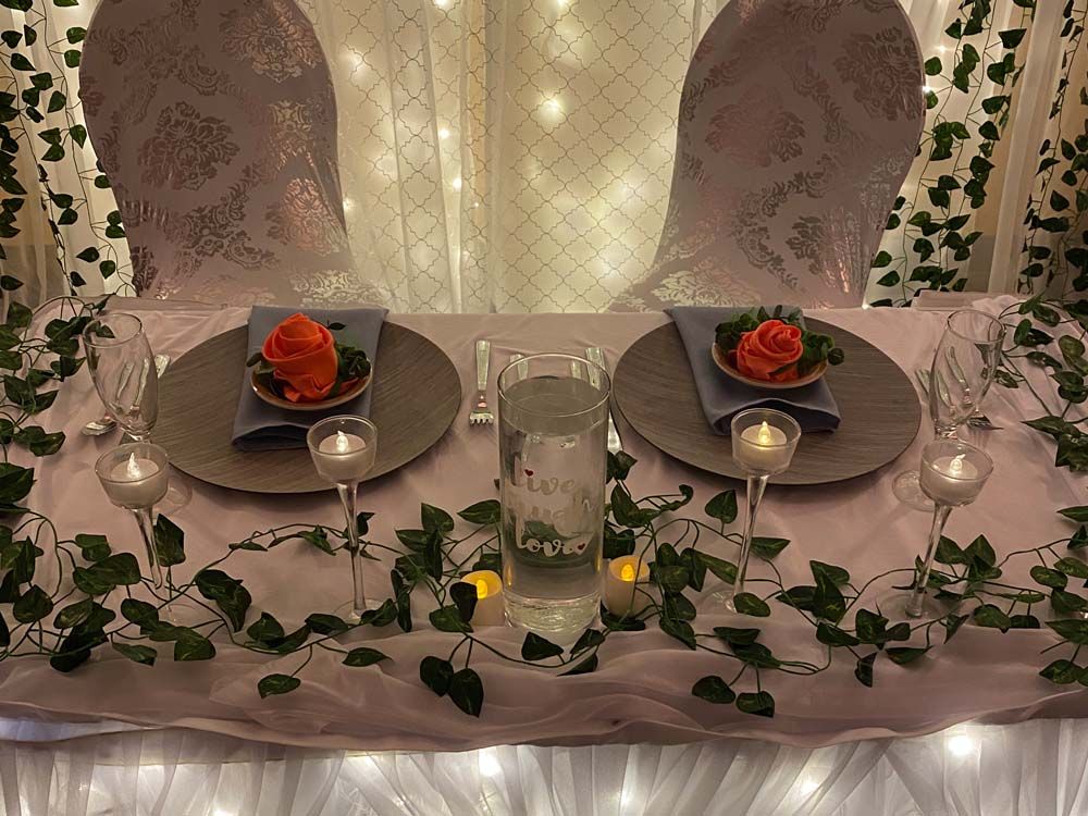 Romantic table setting with rose petals, candles, and two plates in a softly lit tented space