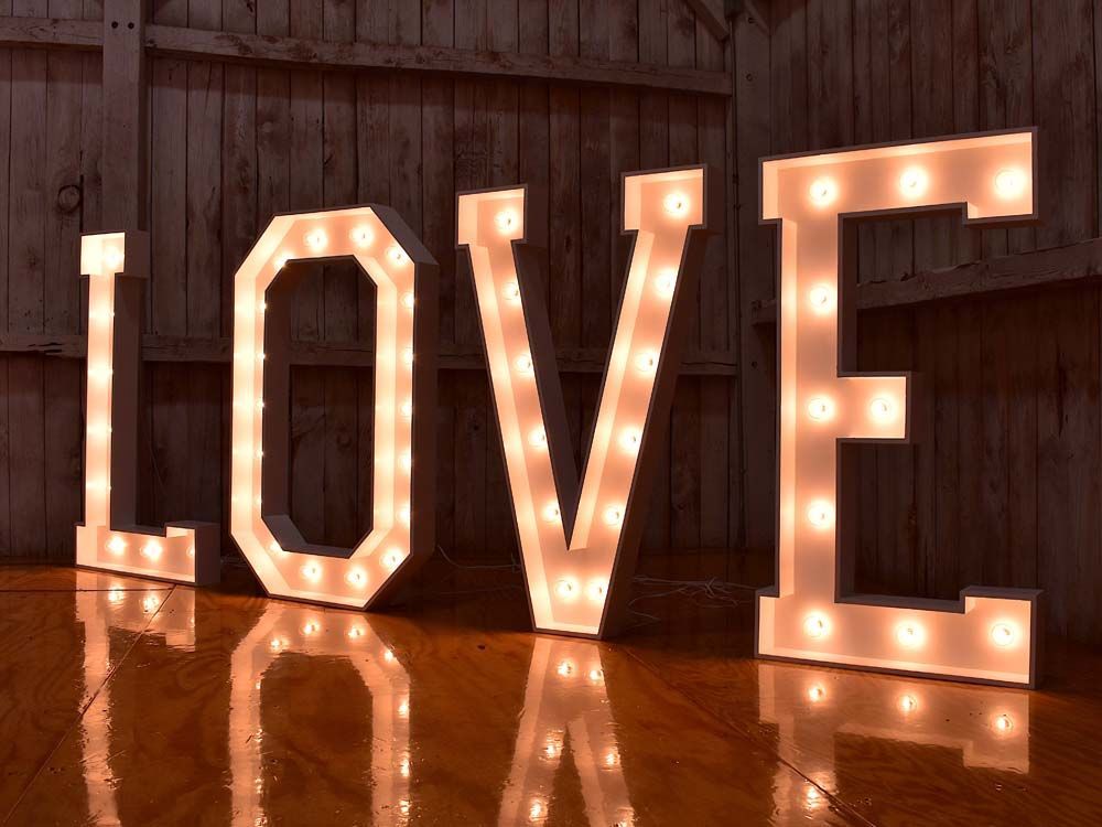 Marquee letters spelling “LOVE” glowing warmly on a wooden floor against a rustic wall.