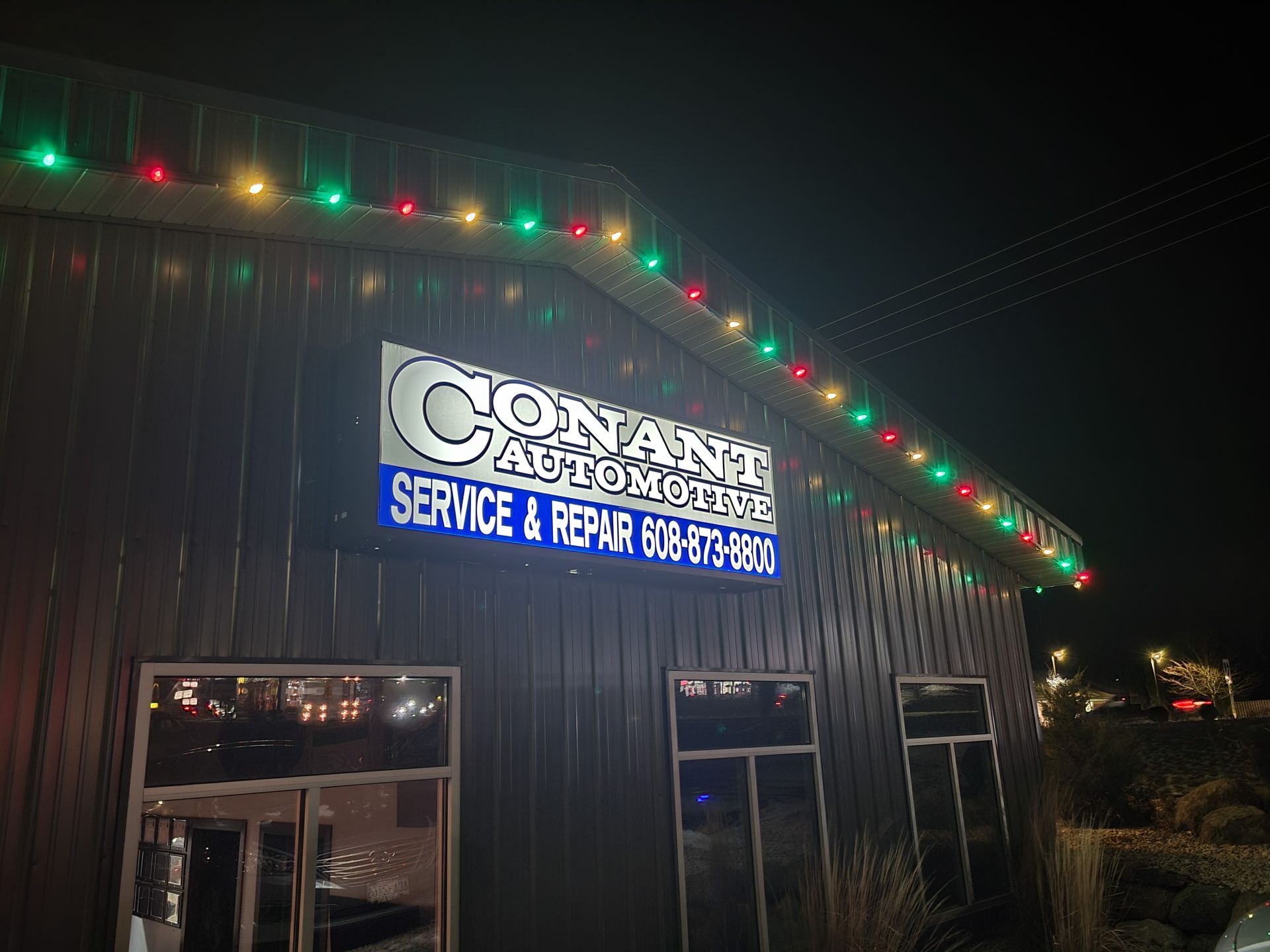 Nighttime exterior of Conant Service & Repair shop with colorful roof lights and illuminated sign.
