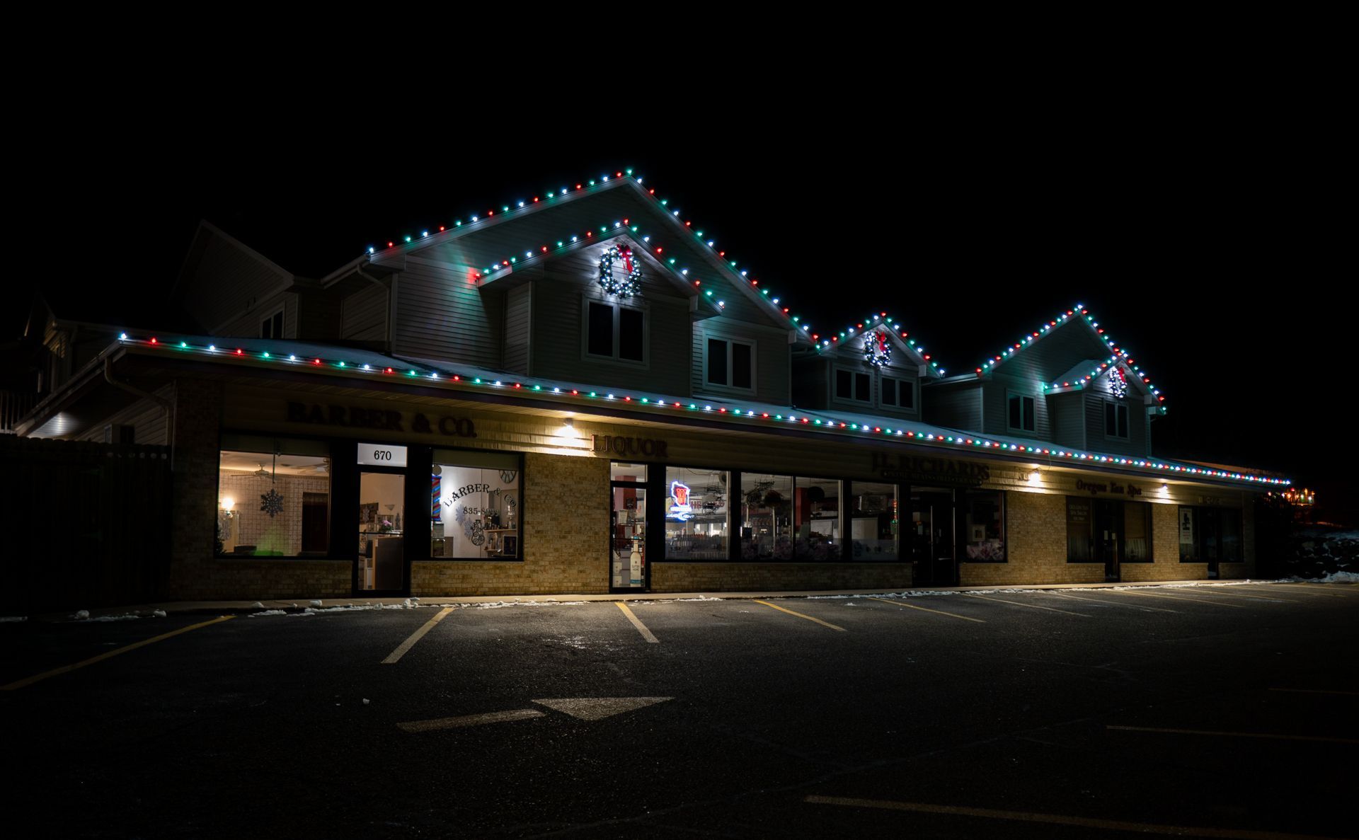 Nighttime exterior of a lit brick building with Christmas lights along the roofline.