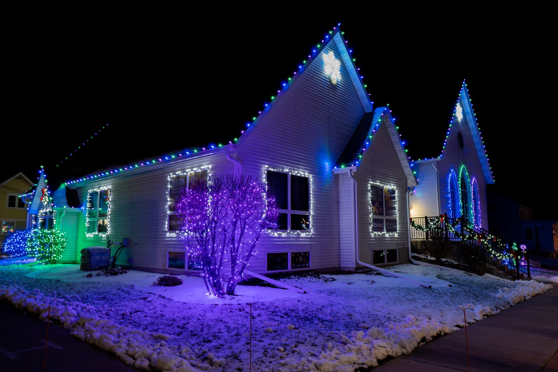Snowy house decorated with blue and purple holiday lights at night