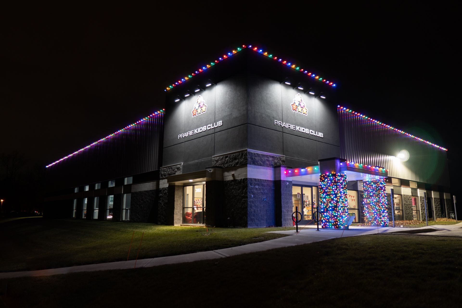 Nighttime view of a lit building with purple roof lights and a decorated entrance