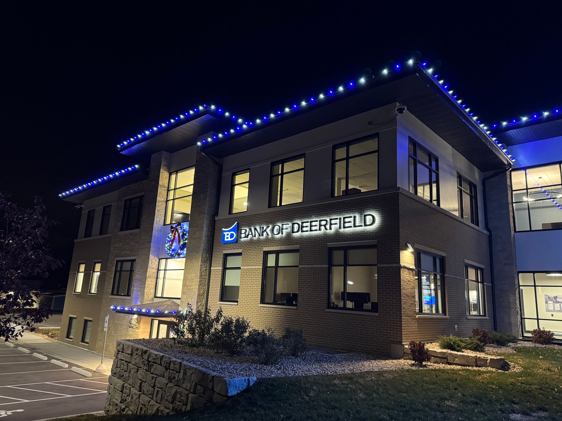 Nighttime view of a two-story office building with blue roof lights and a sign reading “BANK OF THE BLUE.”