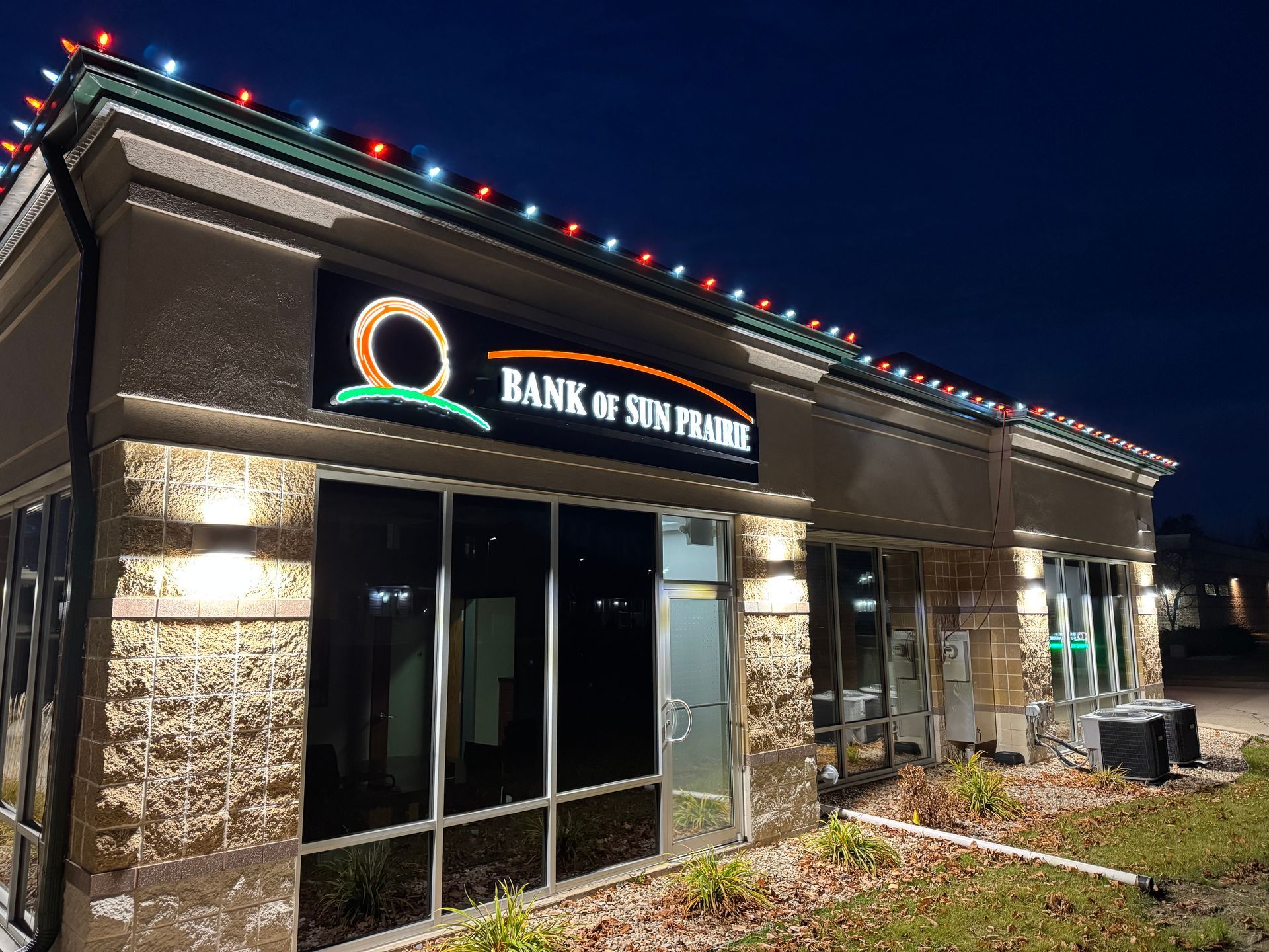 Bank of Sun Prairie branch at night, lit by colorful roof lights and front windows.