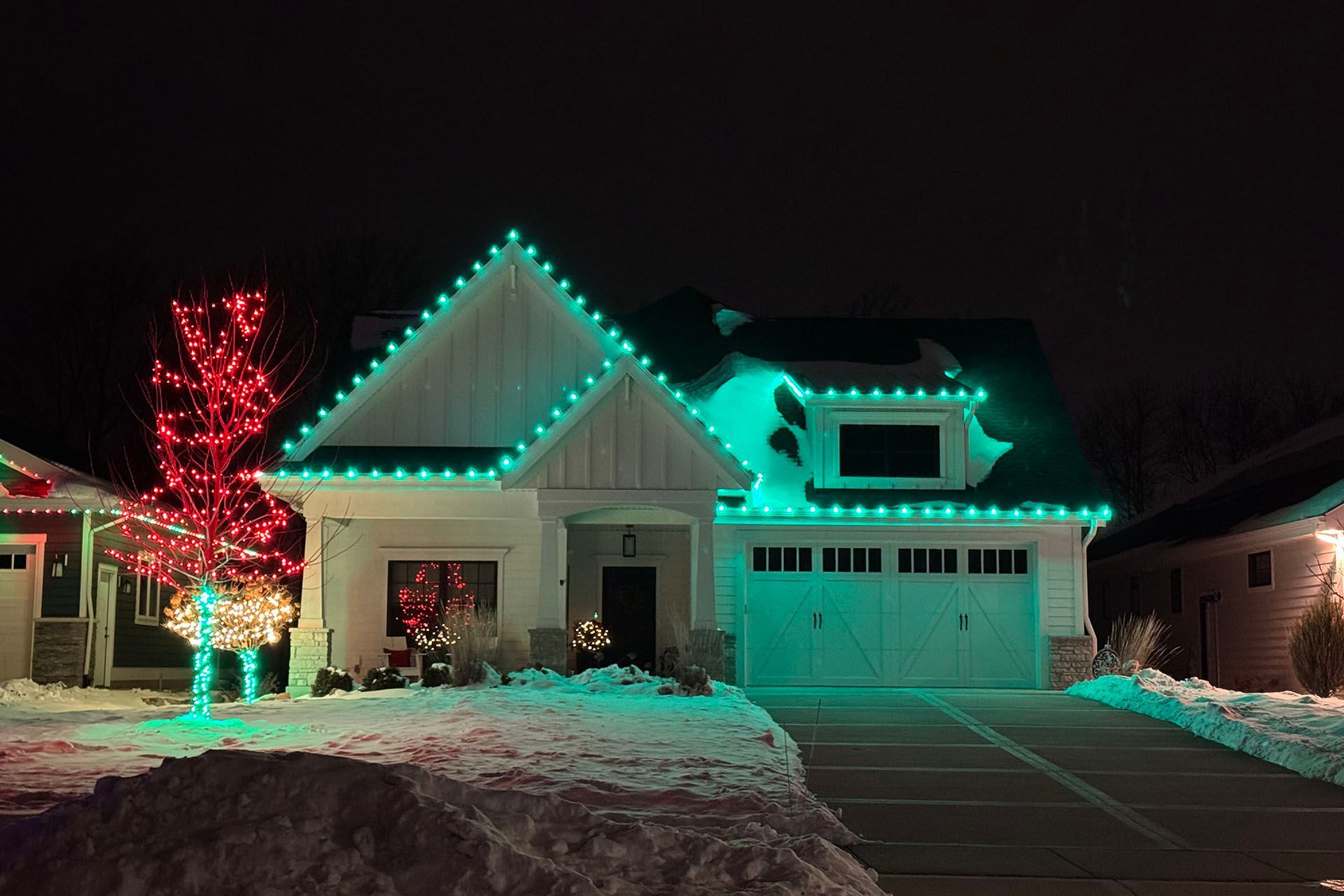 Snowy suburban house decorated with teal and red Christmas lights at night
