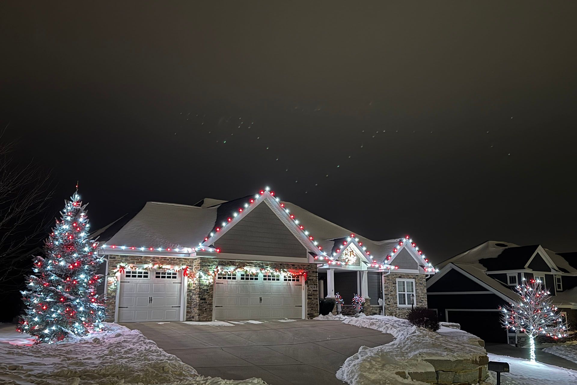 Snowy suburban house decorated with colorful Christmas lights at night