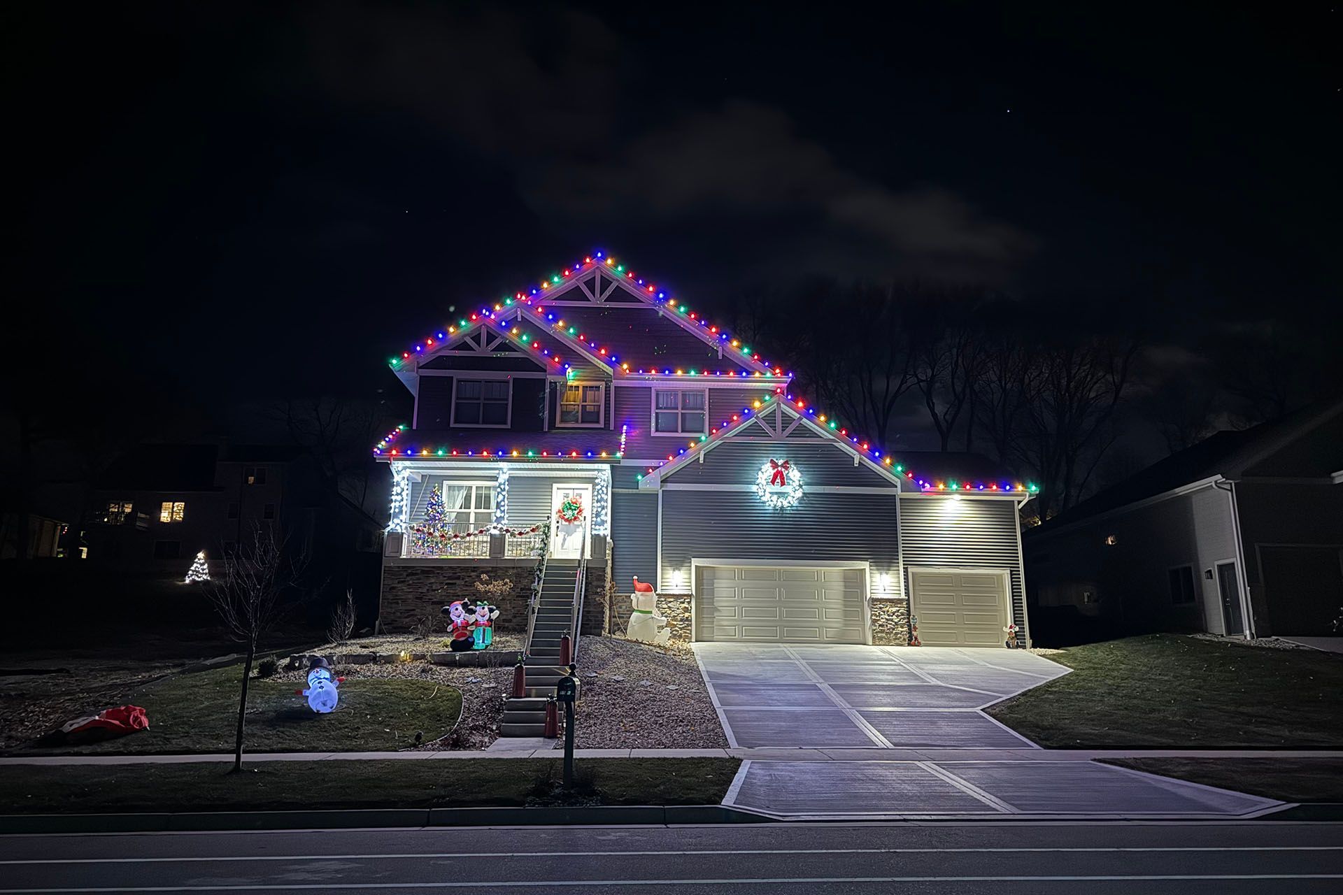House at night decorated with colorful Christmas lights and a lit driveway