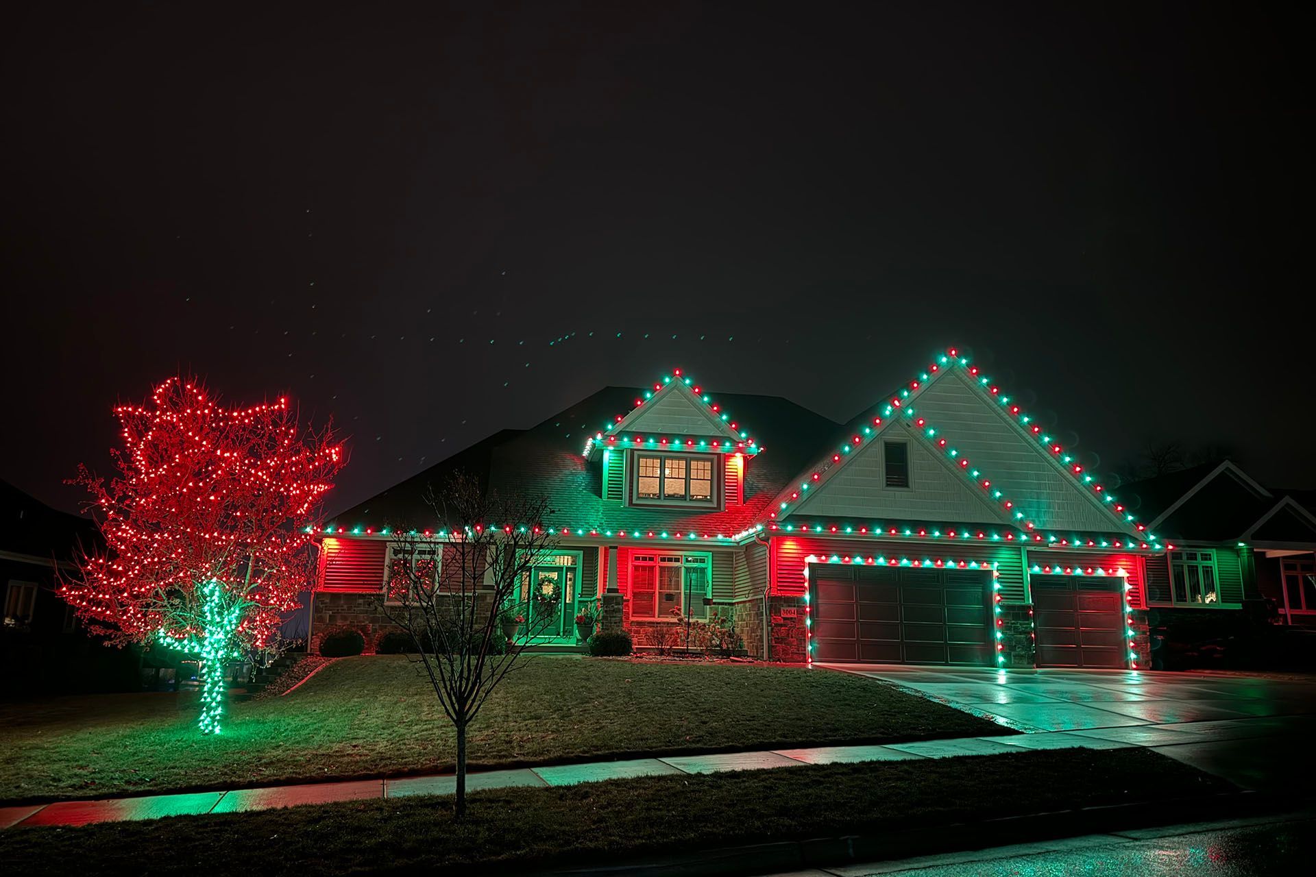 House decorated with red and green Christmas lights on a dark, wet night