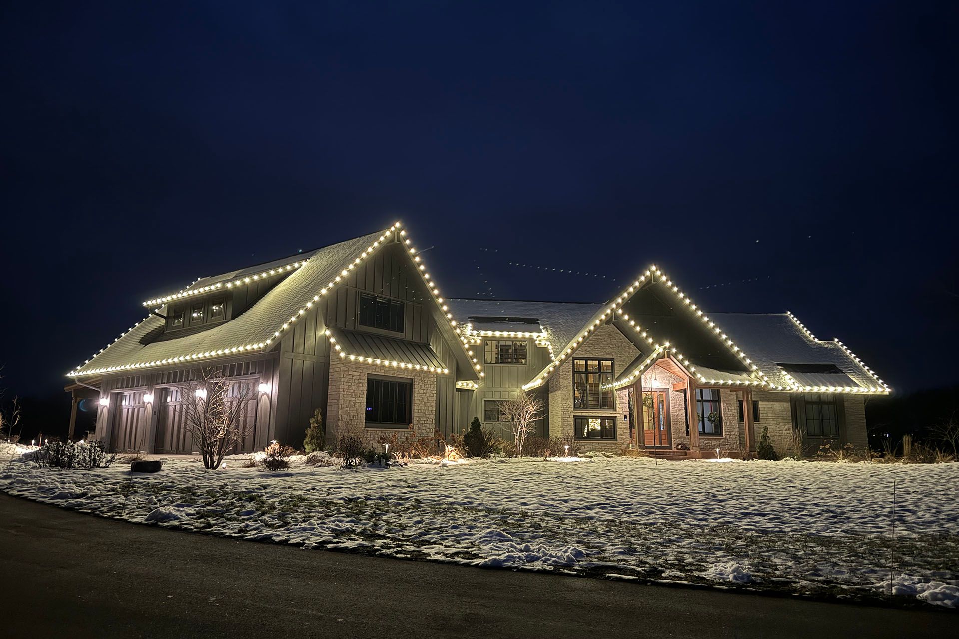 Snow-covered house outlined with warm white holiday lights at night